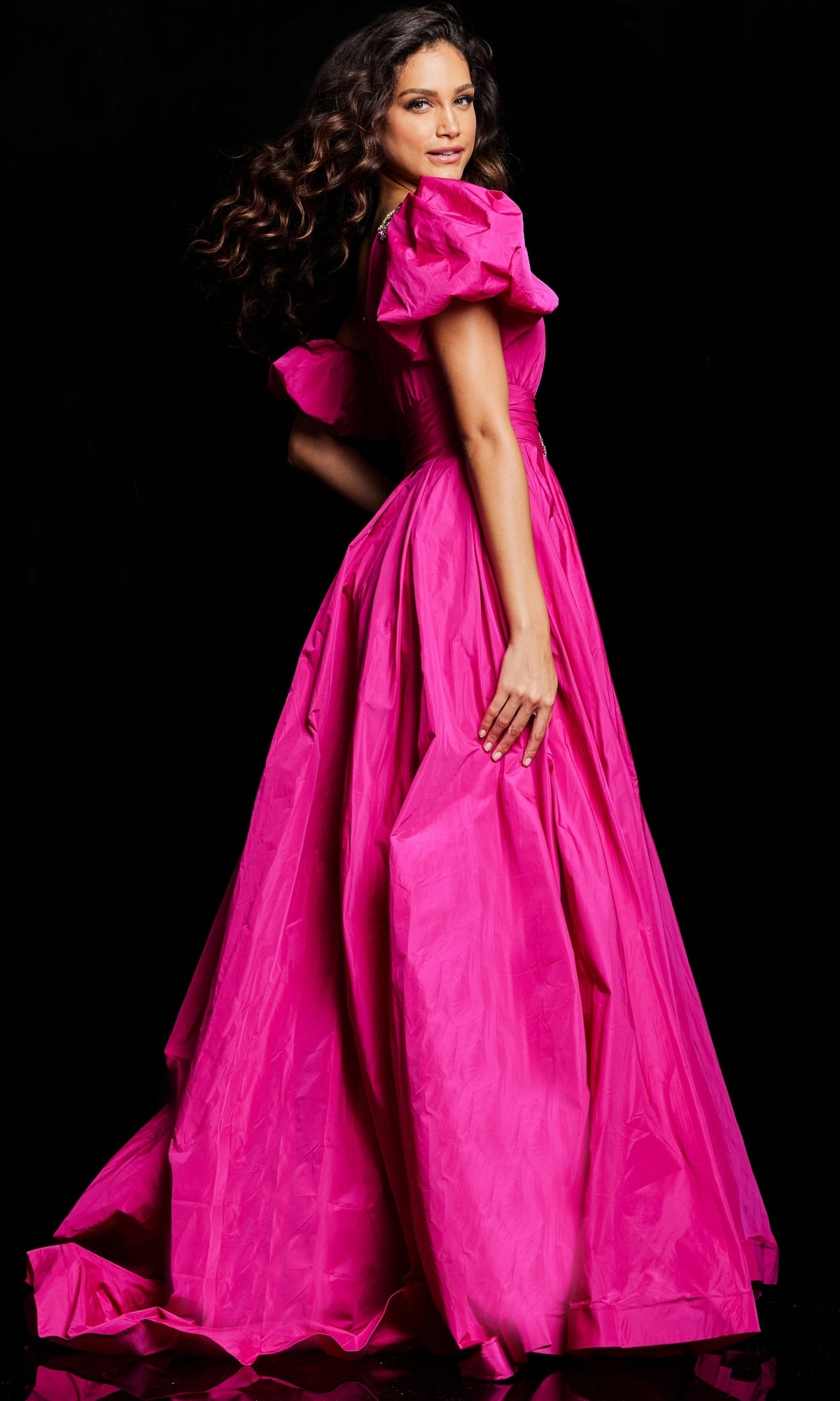 A woman wearing the Long Prom Dress 36872 by Jovani, a bright pink ball gown with puffed sleeves, stands against a black background.