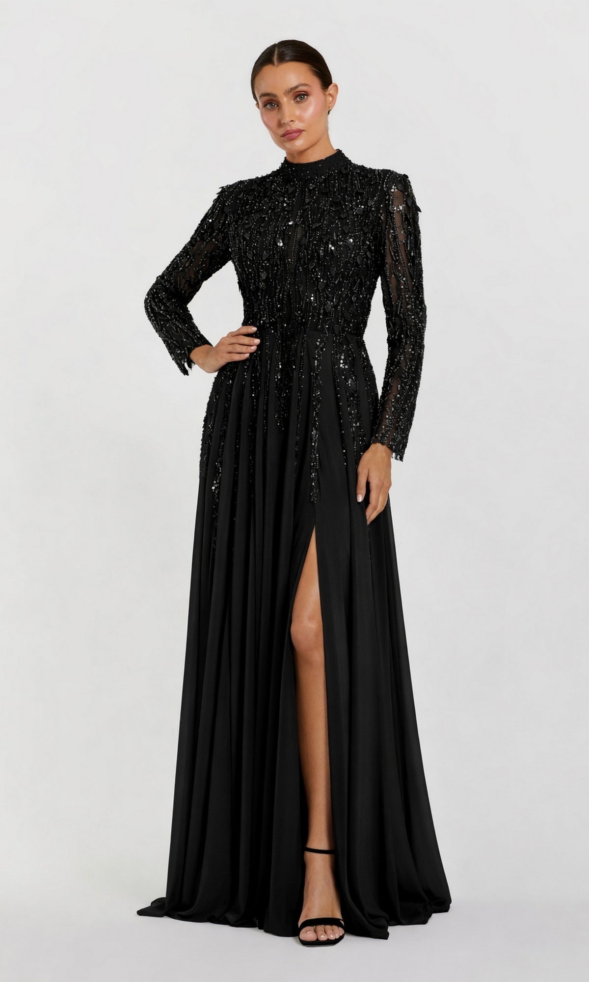 Model wearing the Long Formal Dress: Mac Duggal 37037, a stunning black gown featuring sequin details, long sleeves, and a high slit. The look is completed with black strappy heels against a plain white background.