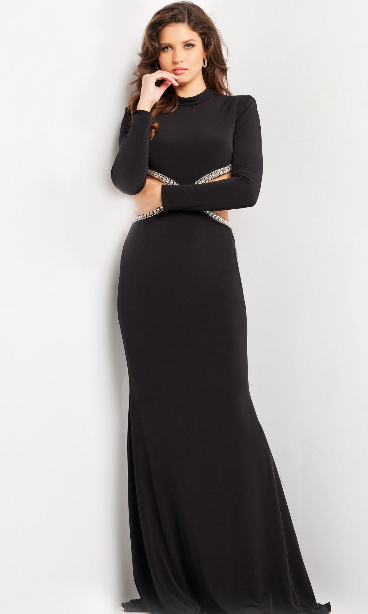 A woman with long brown hair wears the Jovani Long Prom Dress 37037, a fitted jersey gown with long sleeves and jeweled waist cut-outs, standing against a plain white background.
