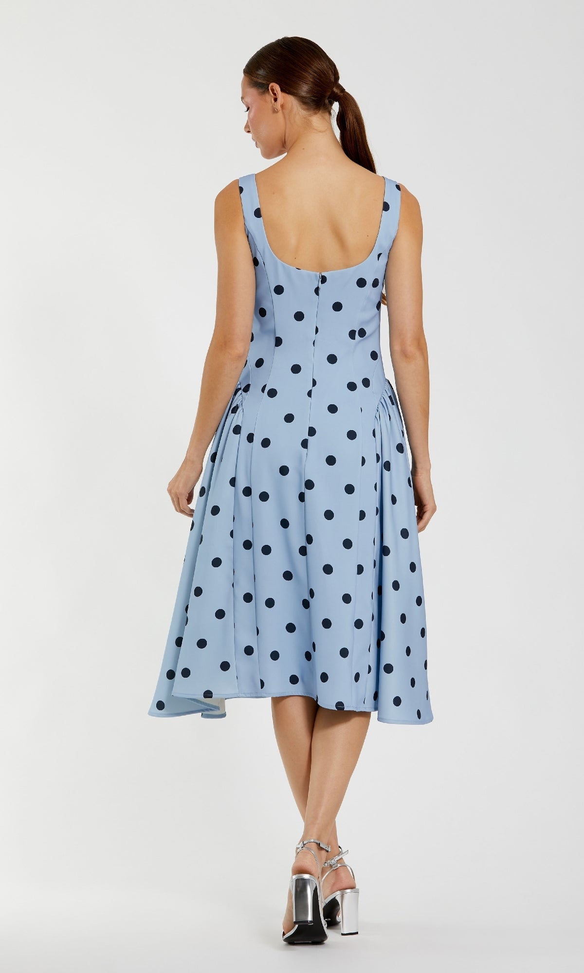 A woman is seen from the back wearing the Mac Duggal 37053 Polka-Dot Wedding-Guest Dress in sky blue with black polka dots and silver high-heeled sandals.