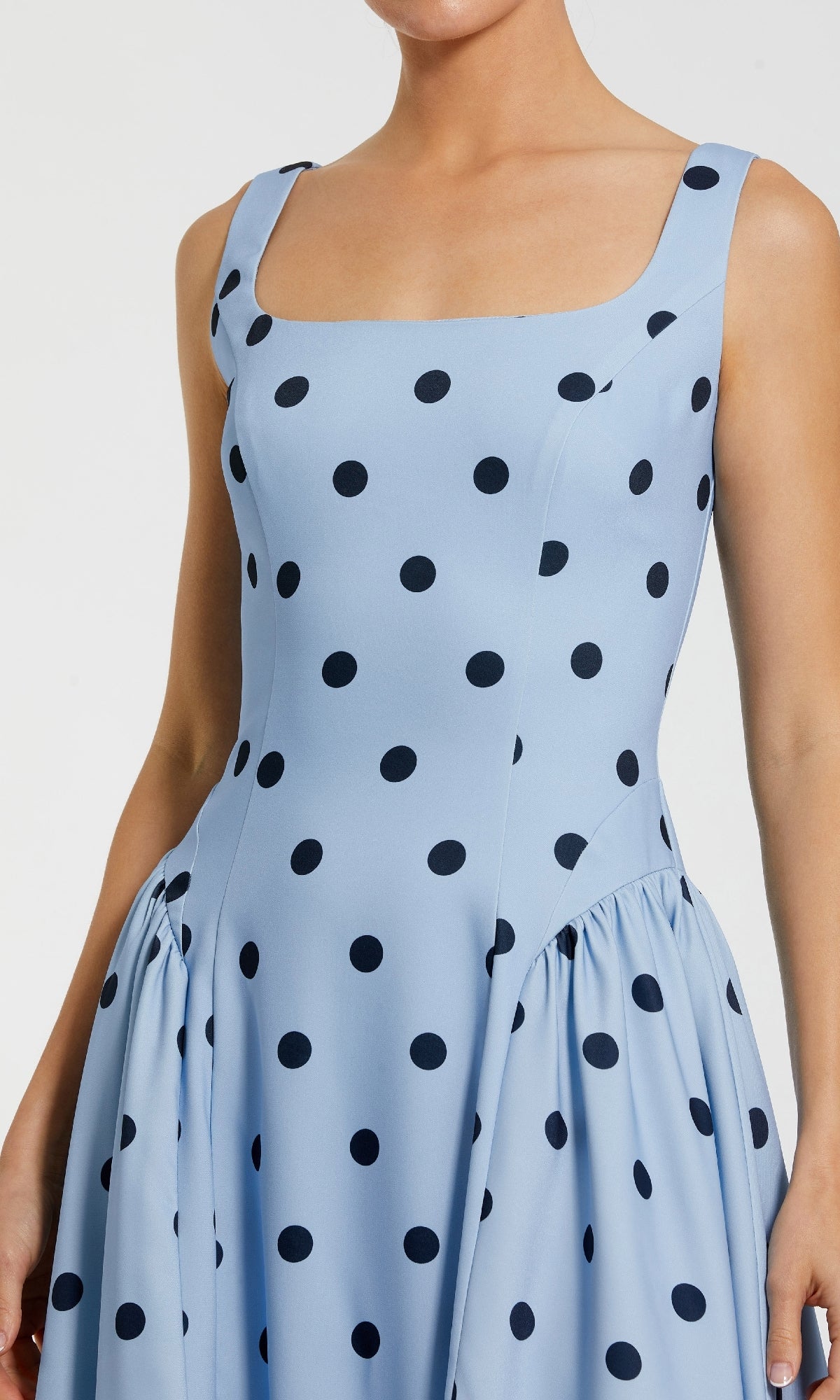 A woman wears the Polka-Dot Wedding-Guest Dress: Mac Duggal 37053—a sleeveless, sky blue midi with a square neckline and black polka dots—perfect for parties or a chic wedding-guest look.