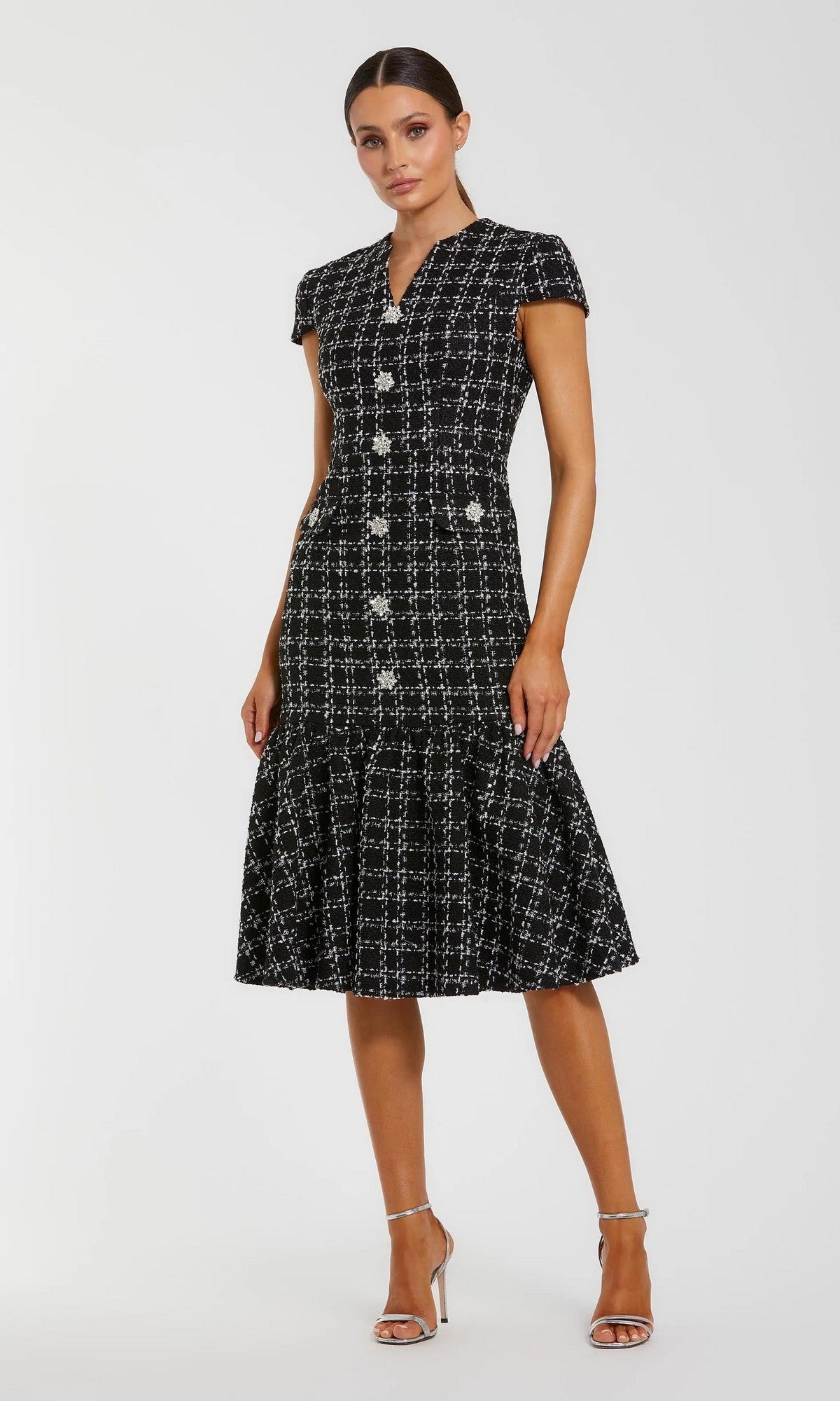 A woman in the Mac Duggal 37071 semi-formal midi day dress, featuring black and white tweed with embellished buttons and a flared hem, pairs it with silver high-heeled sandals against a plain background.