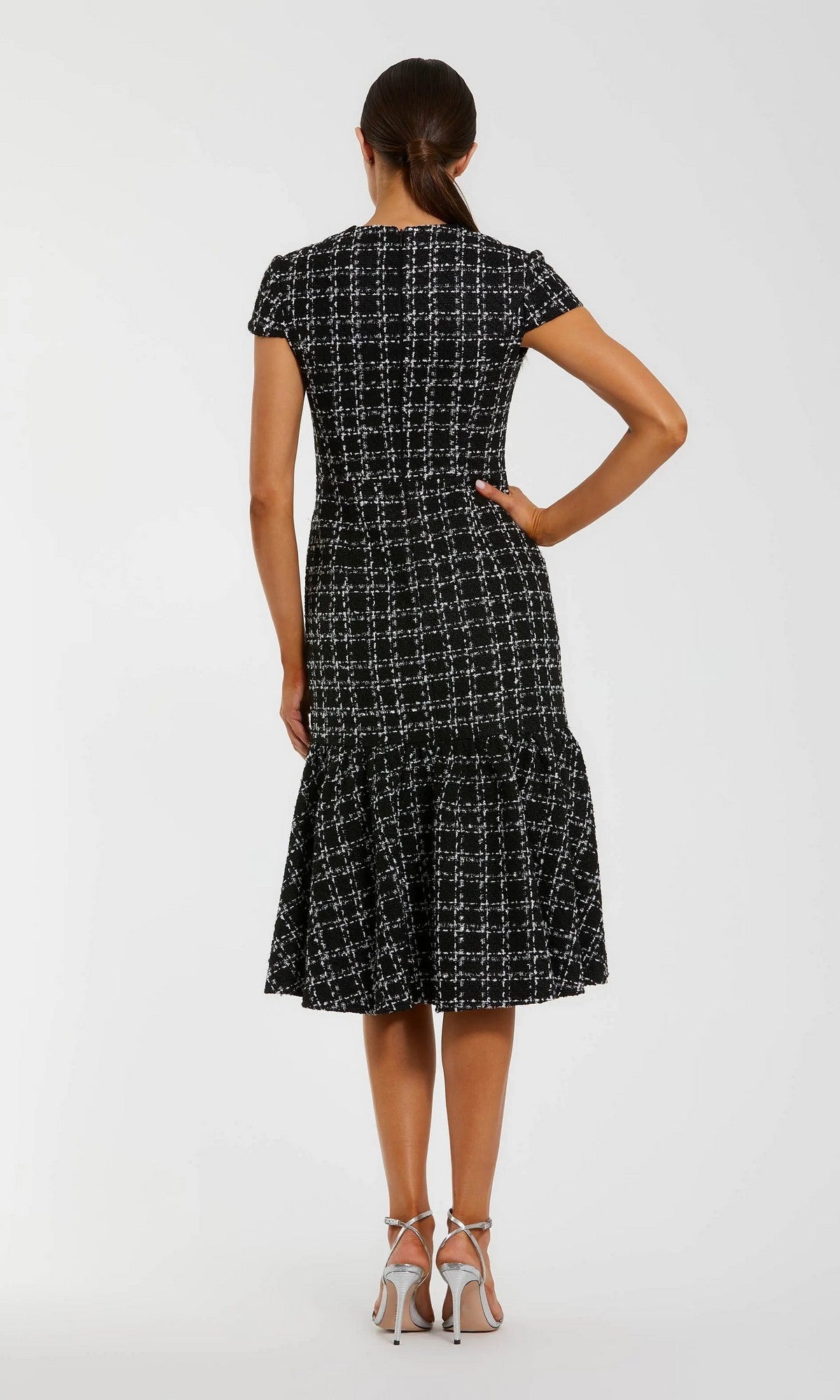 Woman stands with her back to the camera, wearing the Mac Duggal 37071 semi-formal midi day dress—short-sleeve, black and white plaid—with white heeled sandals.
