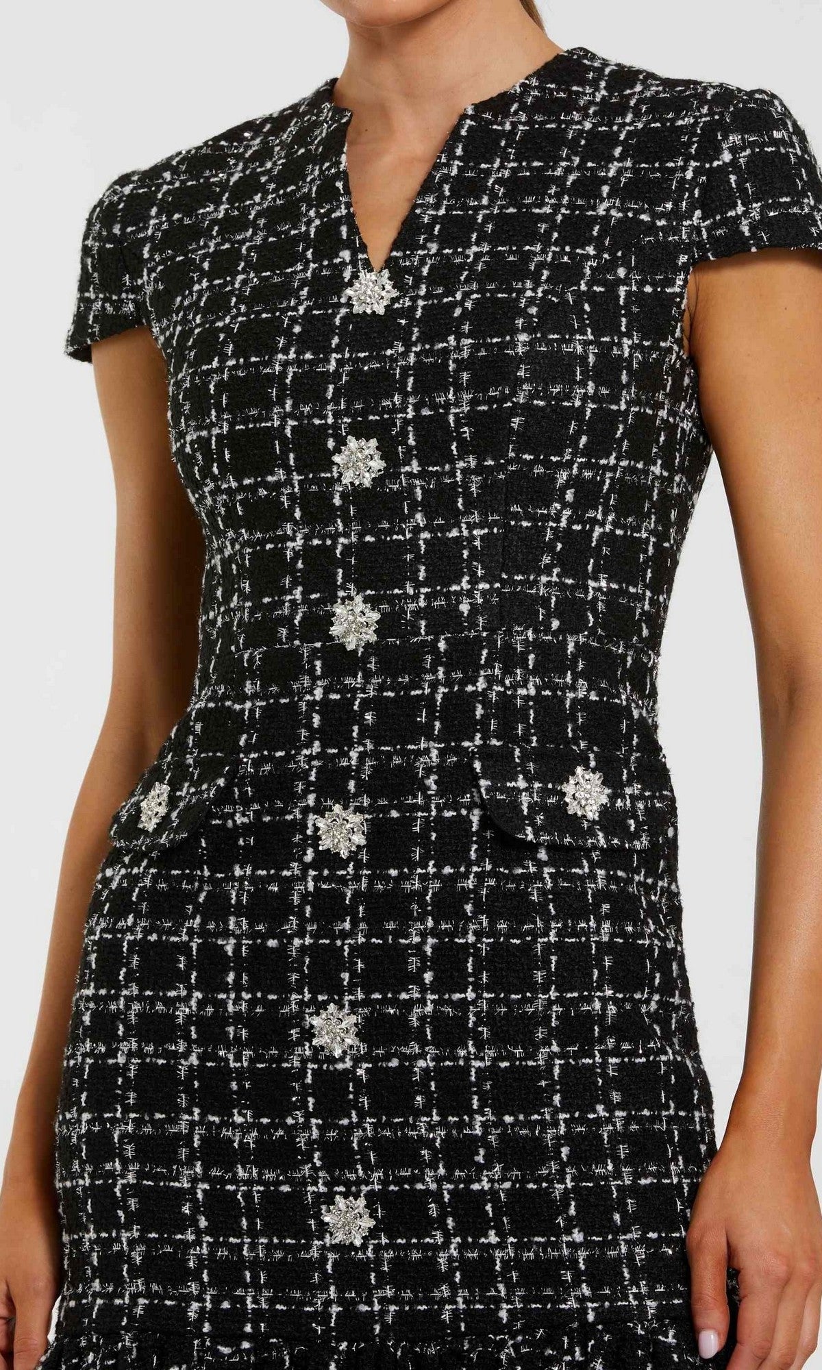 A woman wears the Mac Duggal 37071 Semi-Formal Midi Day Dress, featuring short sleeves, black and white plaid, embellished buttons, and decorative flap pockets; shown from shoulders to above the knees.
