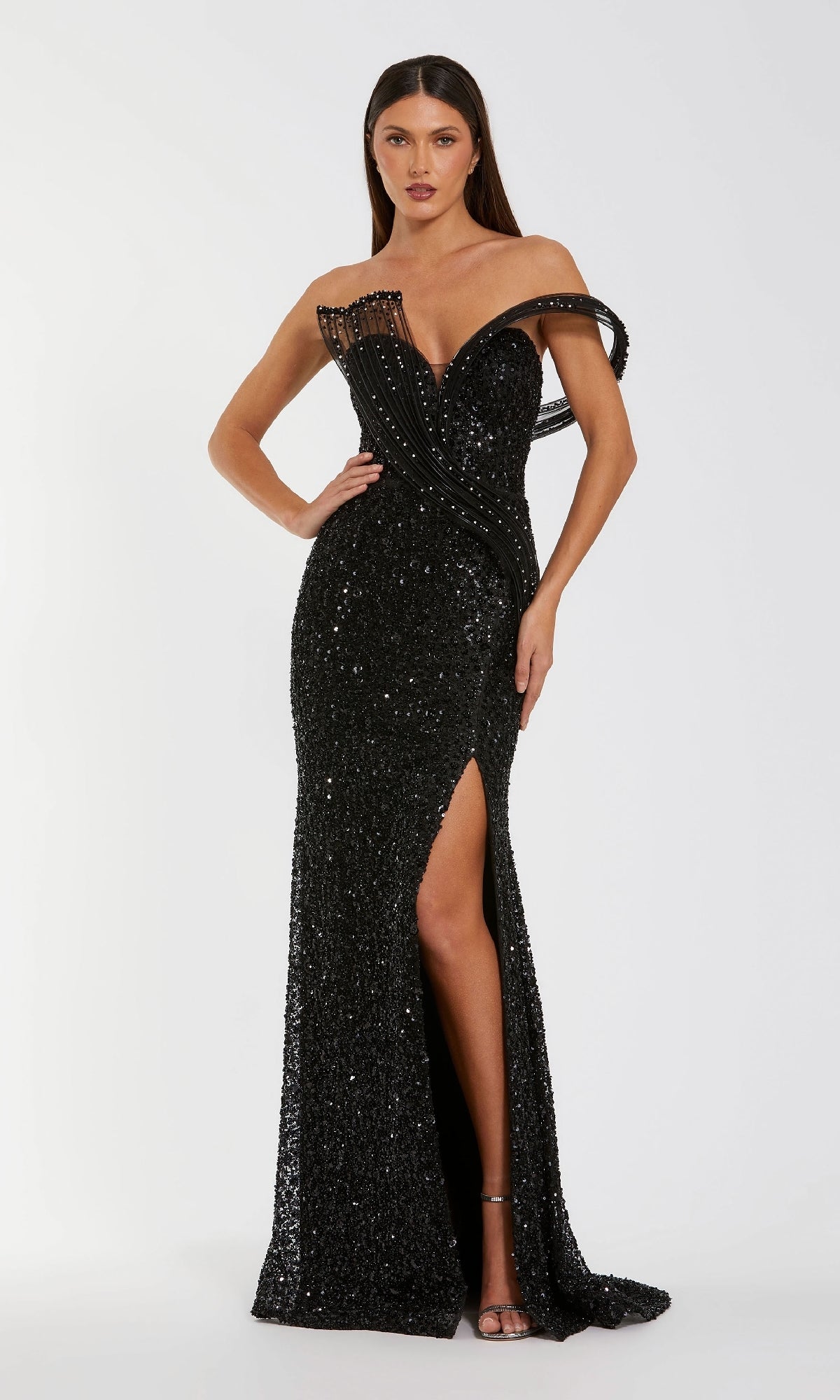 A woman poses against a plain white background wearing the Mac Duggal 37085 long formal dress—a black sequin, off-the-shoulder evening gown with a floor-length silhouette, thigh-high slit, and decorative strap detail.