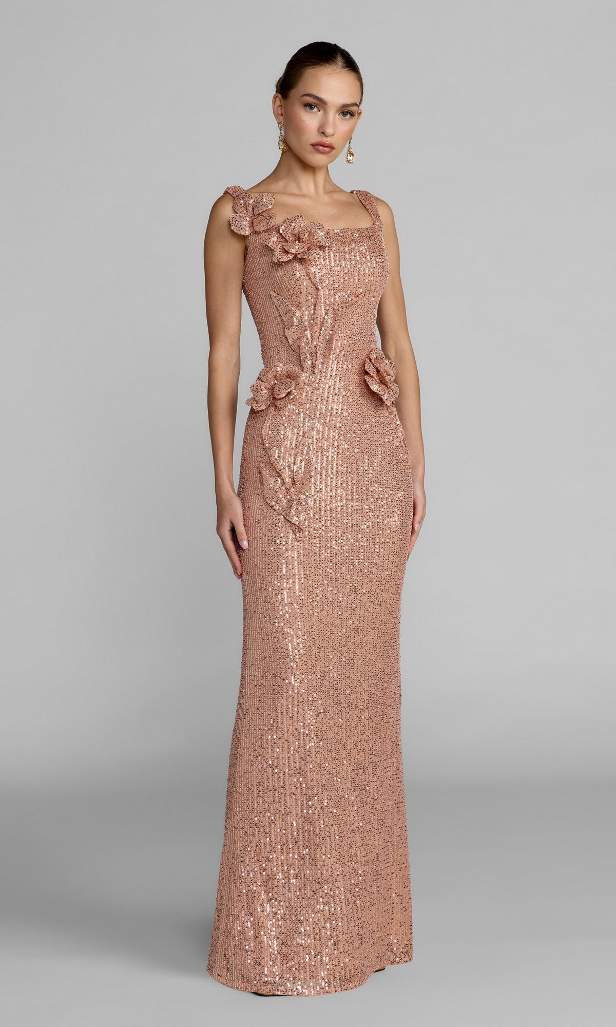 A woman wearing the Mac Duggal 37104 long formal dress in a fitted, sleeveless copper design with floral appliqués on the bodice and waist, posing against a plain gray background.