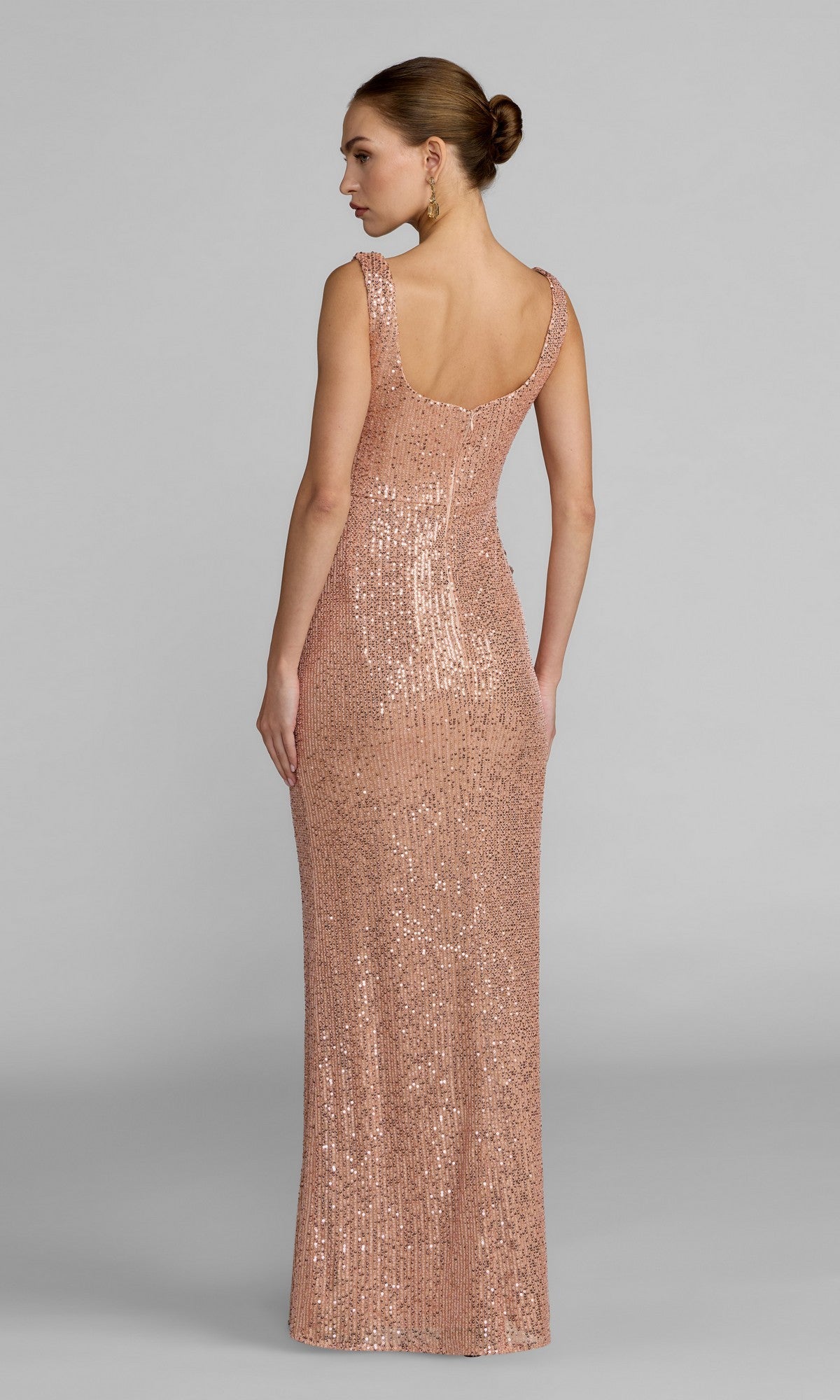 A woman is shown from behind, wearing the Mac Duggal 37104 long formal dress—a sleeveless, floor-length sequin gown with a scoop back—standing against a plain gray background.