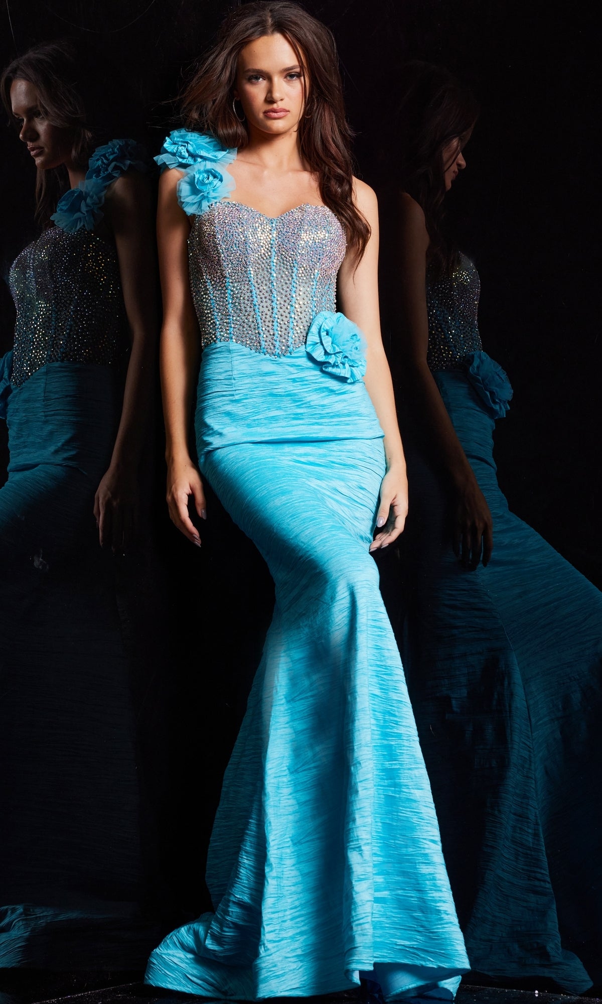 A woman wears the Jovani Long Prom Dress 37268, a fitted one-shoulder mermaid gown with floral accents and an embellished corset bodice, standing in front of a reflective surface.