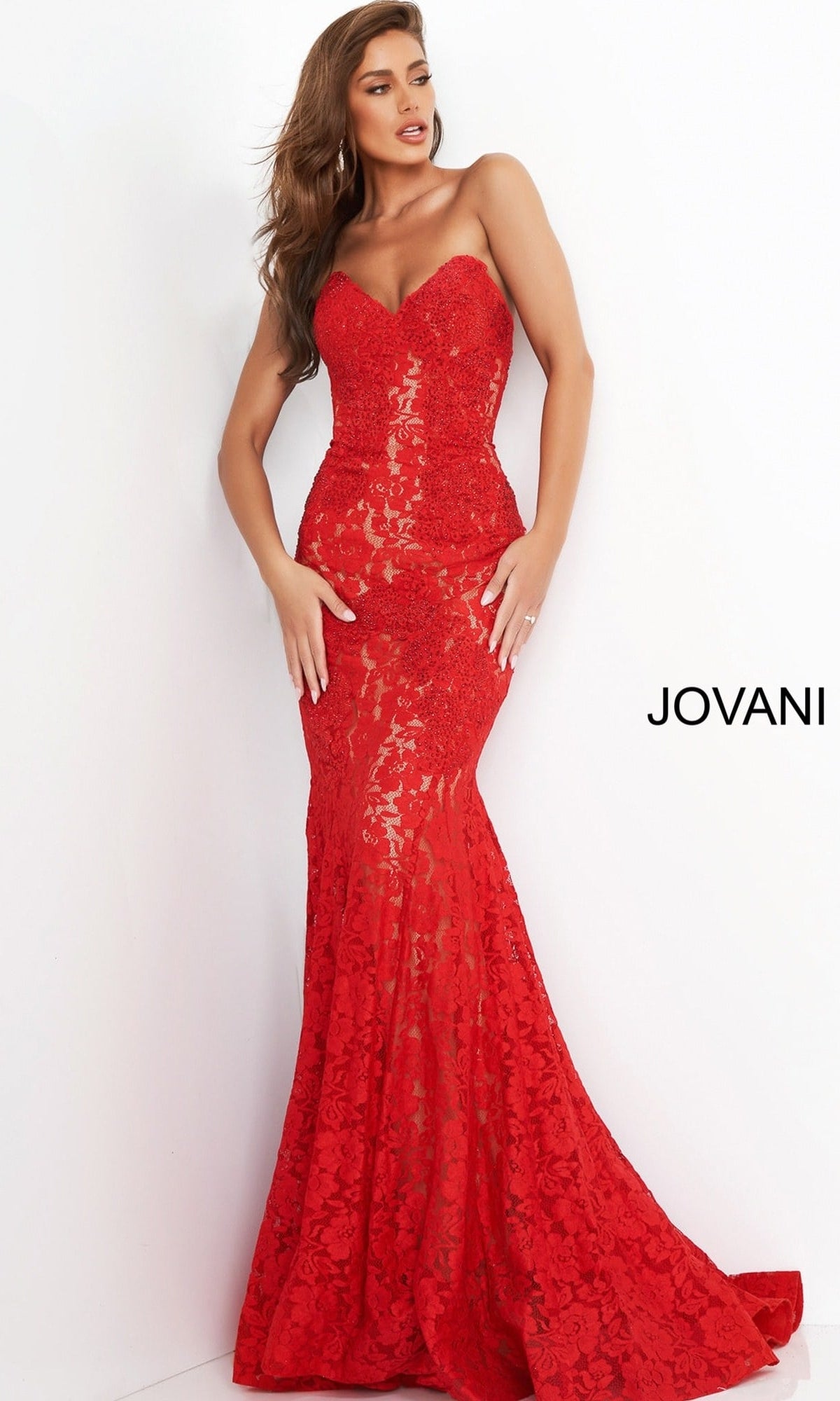 A model wearing a Strapless Long Lace Prom Dress; Jovani 37334, a floor-length red lace gown with a sweetheart neckline and a mermaid silhouette.