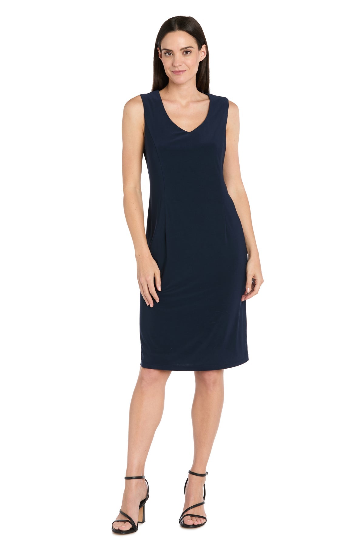 A woman models the R&M Richards 3742 Short Navy Jacket Party Dress, a sleeveless knee-length party dress with a V-neckline, paired with black strappy heels, standing against a white background.