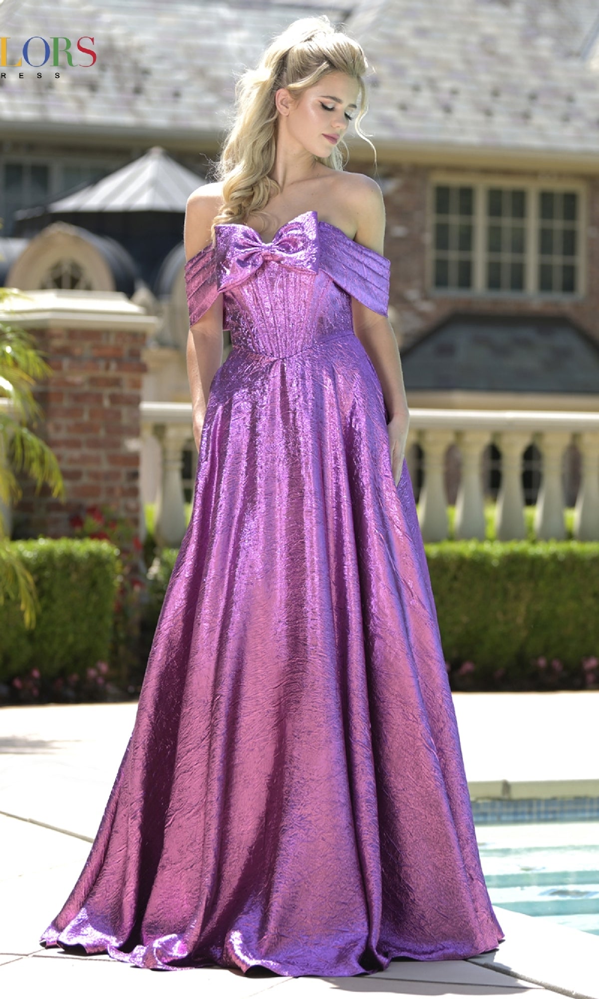A woman in the Off-Shoulder Corset Prom Gown: Colors Dress 3792, a shimmery purple dress, stands by a pool outdoors with a house and lush greenery in the background.