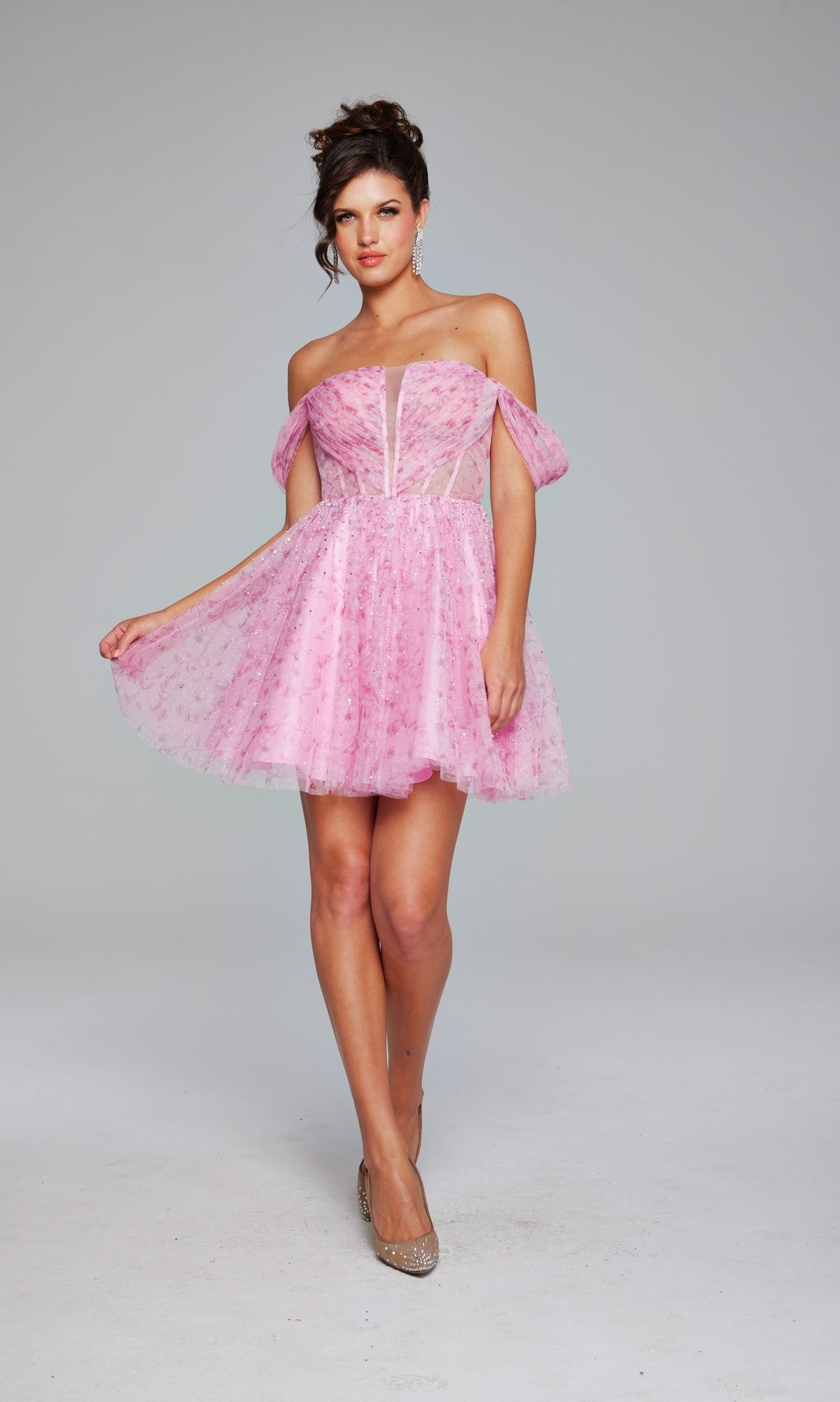 A woman models the Jovani Off-Shoulder Short Pink Hoco Dress 38000, featuring sheer panels and puffed sleeves, set against a plain light gray background.