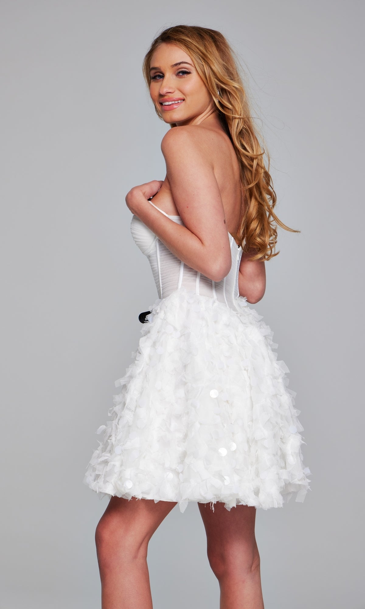 Woman with long blonde hair wears the Jovani Strapless Short White Hoco Dress 38248, featuring a textured ruffled skirt, as she smiles at the camera against a plain background—a chic homecoming look.