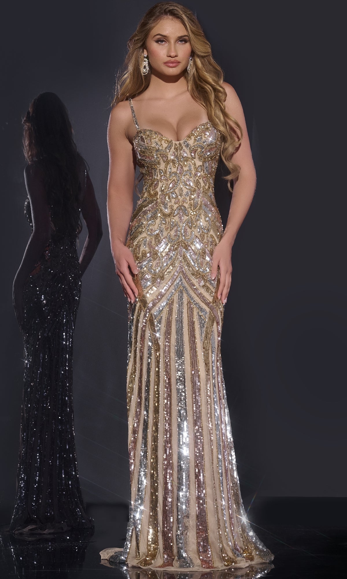 A woman in the Jovani Long Sequin-Print Prom Dress 38300, featuring gold and silver sequins, a fitted bodice, and thin straps, stands against a dark background with her reflection visible behind her.