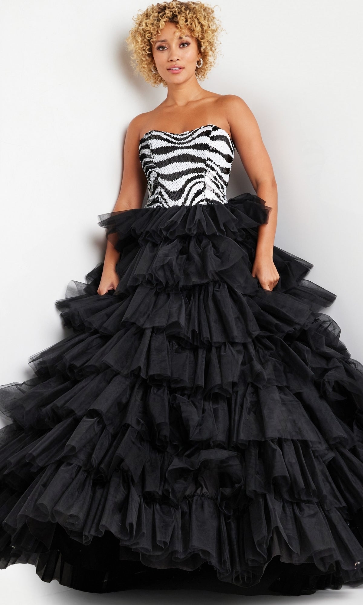 A woman models the Jovani Black White Long Ruffled Prom Dress 38360, featuring a zebra-patterned strapless bodice and a dramatic black ruffled tulle skirt, against a plain background.