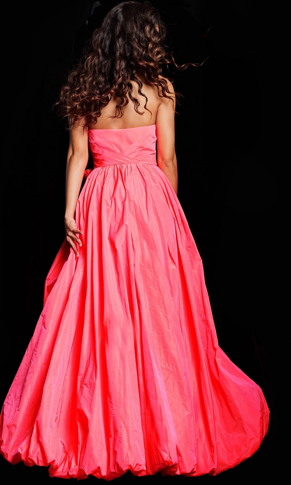 A woman with long curly hair, seen from behind against a black background, wears the Jovani Long Taffeta Bubble Prom Ball Gown 38382.