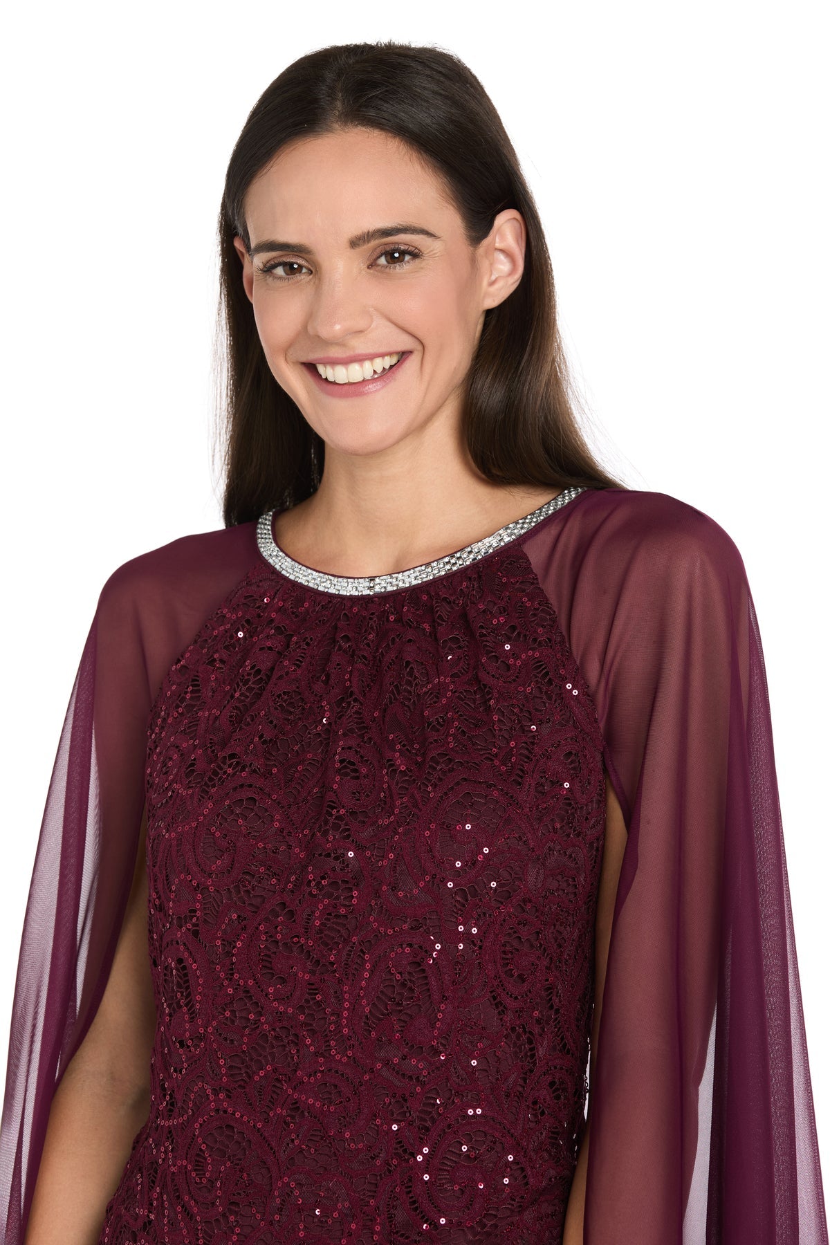 Woman smiling in the R&M Richards 3864 Knee-Length Cape Party Dress with sequin lace, sheer sleeves, and a silver-trimmed neckline, set against a white background.