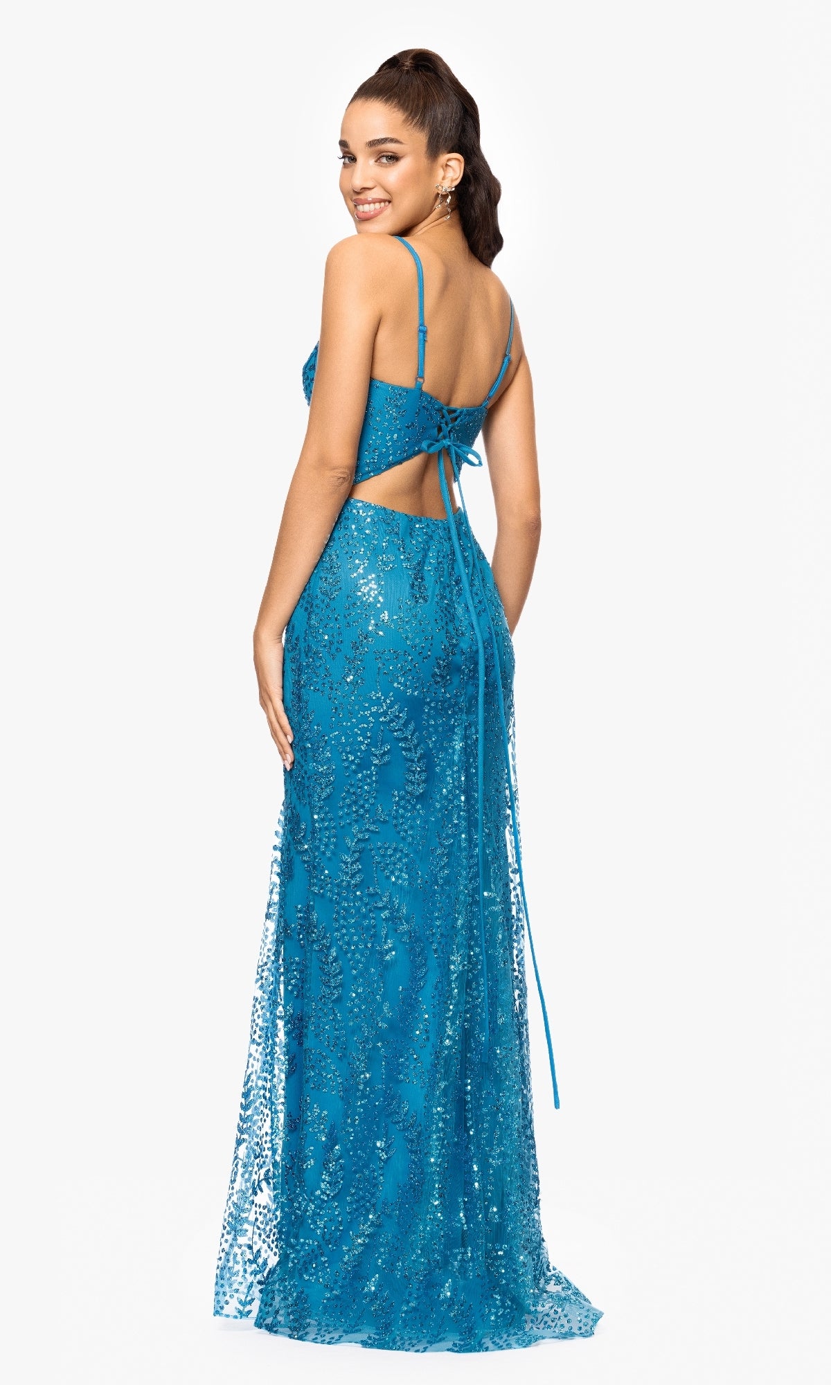 A woman poses and smiles over her shoulder in the Long Sequin-Print Prom Dress by Blondie Nites 3878BN, a sleeveless, floor-length blue gown with lace details and a cutout back tied with thin straps.