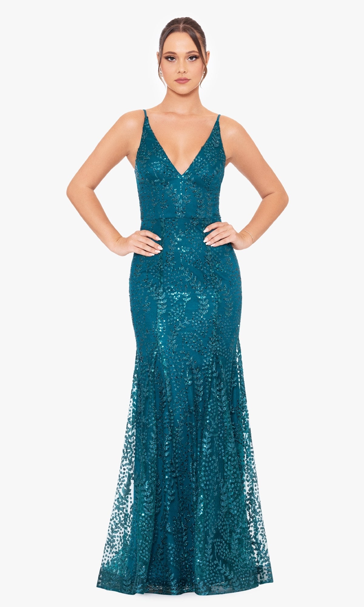 A woman faces forward in the Blondie Nites 3878BN long sequin-print prom dress featuring a deep V-neckline and floor-length teal shimmer, set against a plain white background.