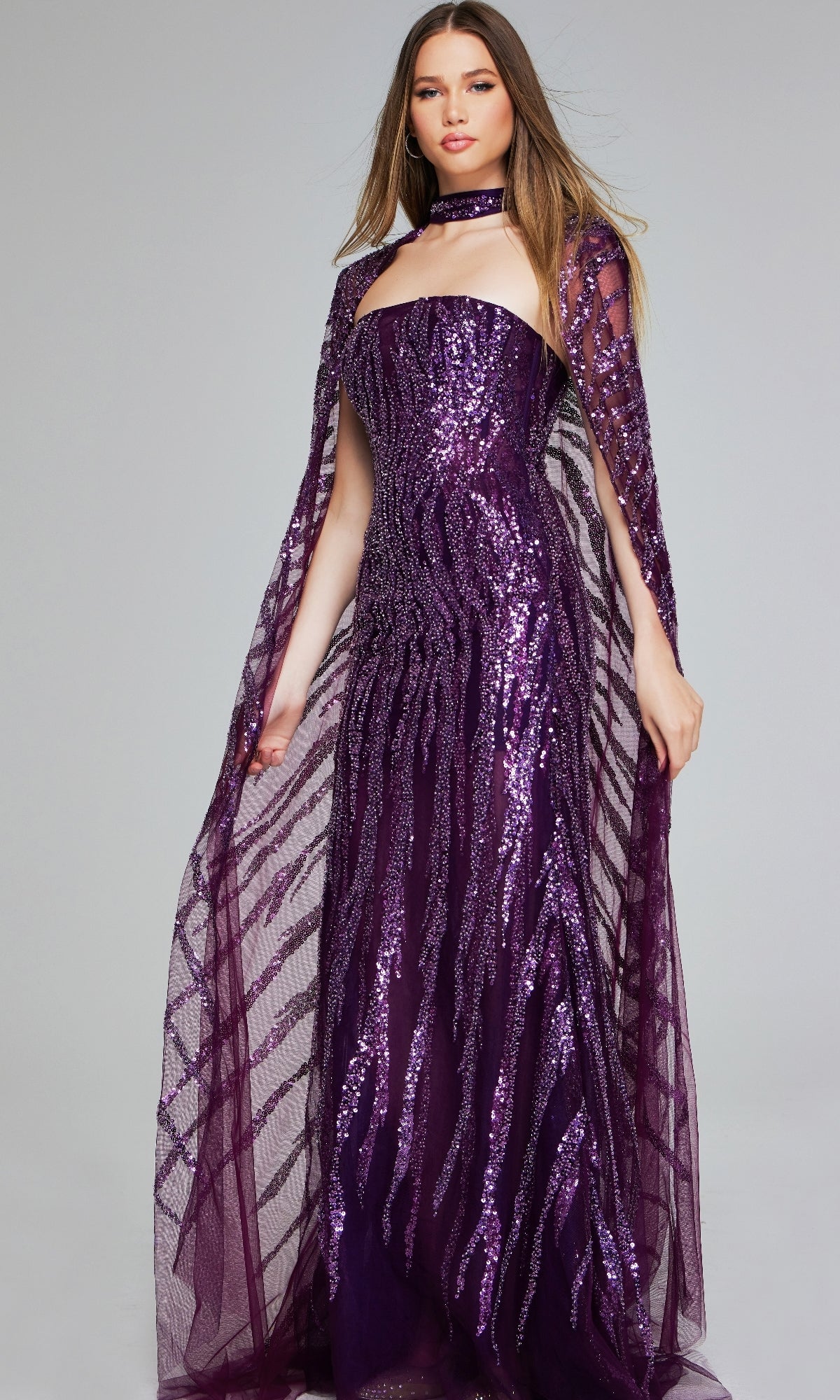 A woman models the Jovani 39046 Purple Sequin Pageant Dress—strapless, floor-length, with a matching sheer cape and choker—against a plain gray background, making it perfect for any special occasion.