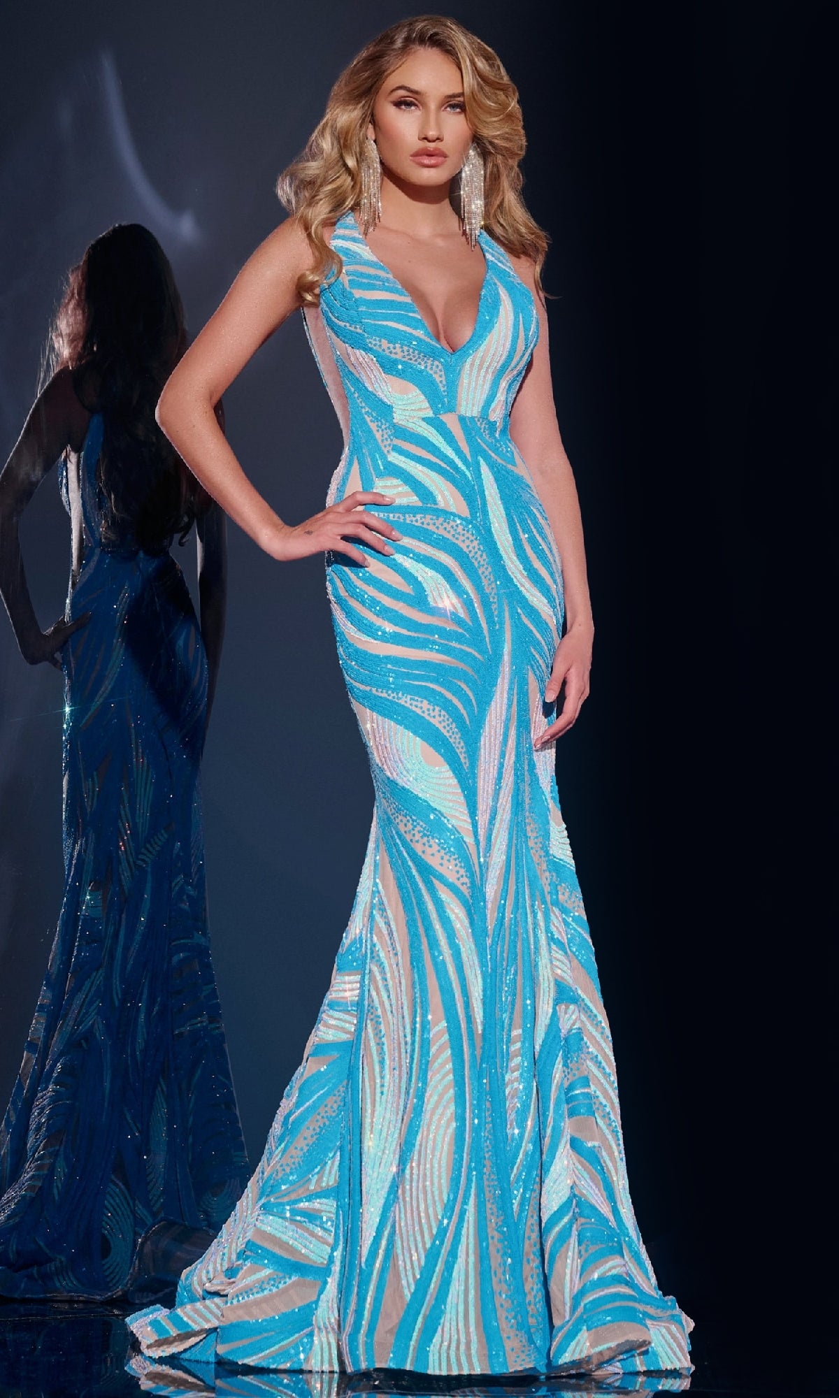 A woman stands beside a mirror in the Jovani 39232 long prom dress—a sleeveless, floor-length blue and white sequin gown featuring a deep V-neckline.