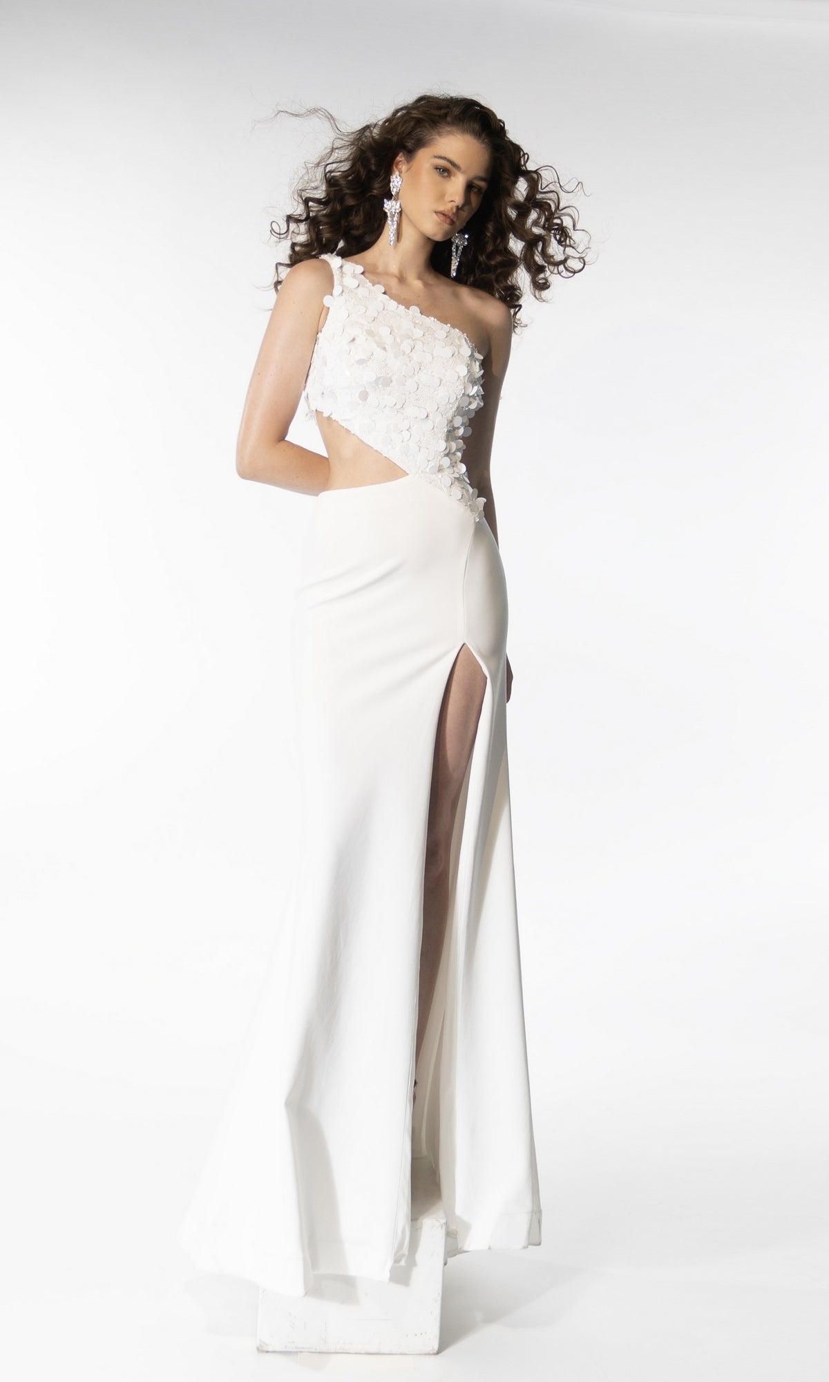 A woman models the Ava Presley 39247, a white one-shoulder long prom dress with floral embellishments, a thigh-high slit, and side cut-out, against a plain white background.