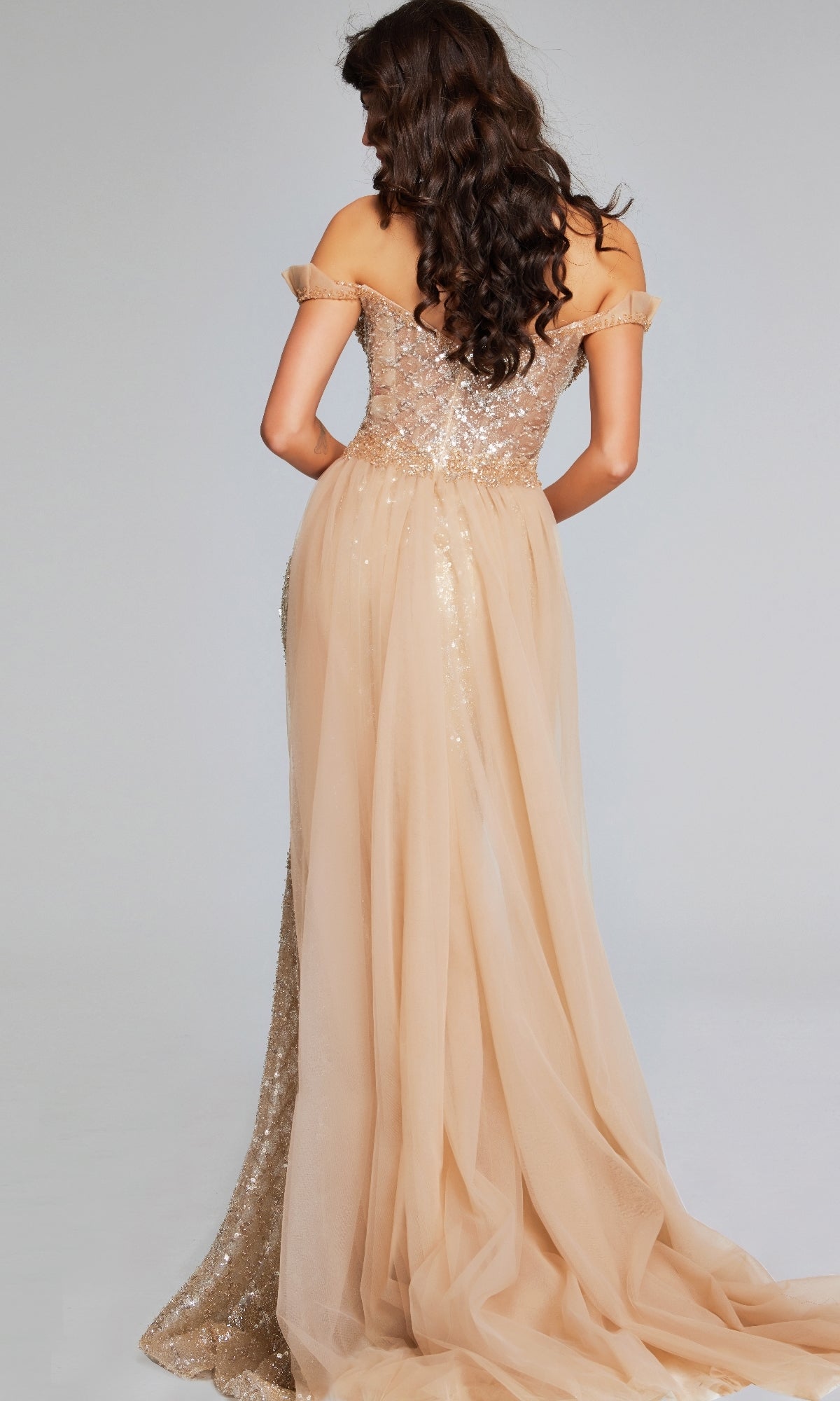 A woman with long, wavy brown hair is seen from behind in Jovani 39389, a floor-length nude sequin mermaid evening gown with tulle accents and an off-the-shoulder design.