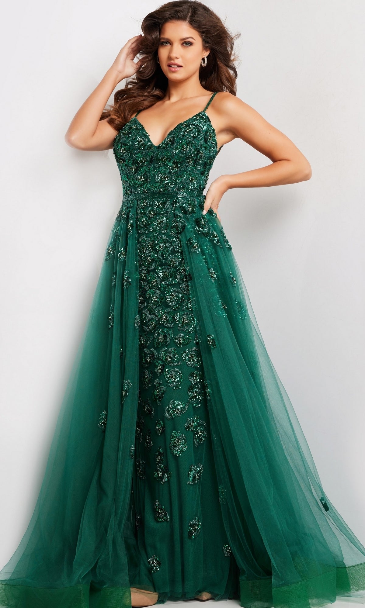 A woman poses in the Long Prom Dress 39434 by Jovani, featuring a sleeveless deep green beaded bodice with a tulle overlay and A-line overskirt, set against a plain light background.