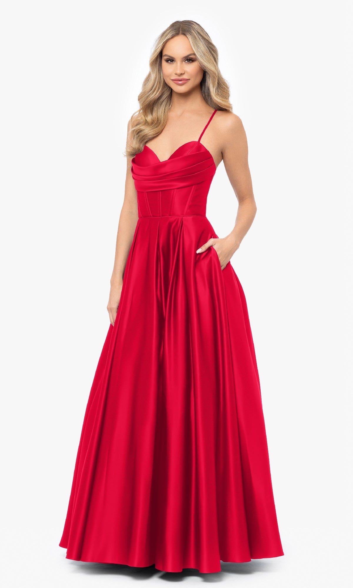 A woman models the Blondie Nites 3946BN Long A-Line Prom Dress—a floor-length, sleeveless red satin gown with thin straps, corset waist, fitted bodice, and pockets—against a plain white background.