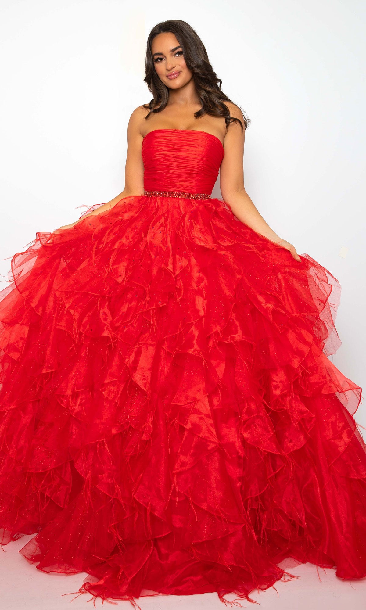 A woman models the Ava Presley 39555 Strapless Ruffle Prom Gown in bright red, showcasing its voluminous ruffled A-line skirt, standing against a plain white background.