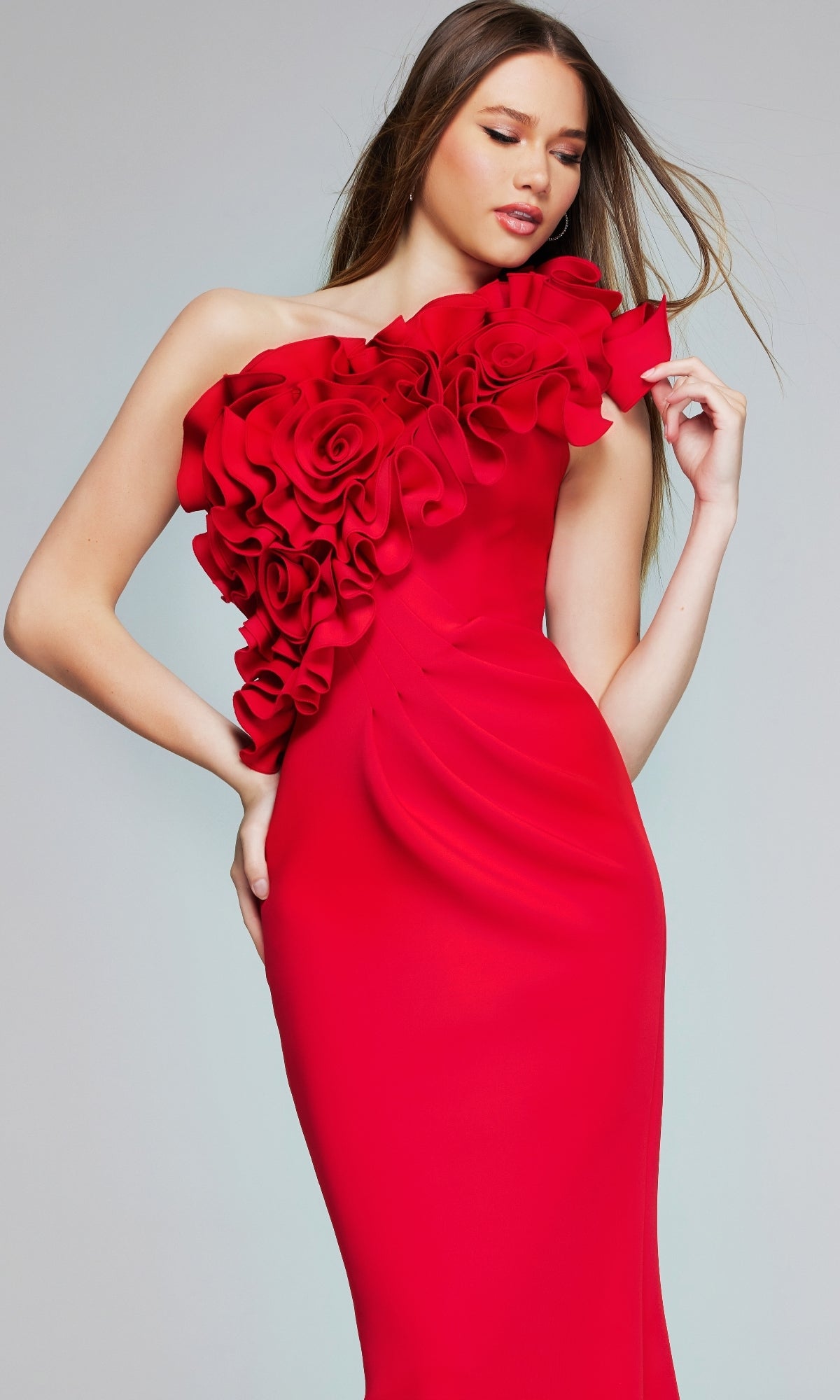 A woman poses against a plain background wearing the Long Formal Dress: Jovani 39751, a fitted red gown featuring a one-shoulder neckline and large floral embellishments on the bodice.