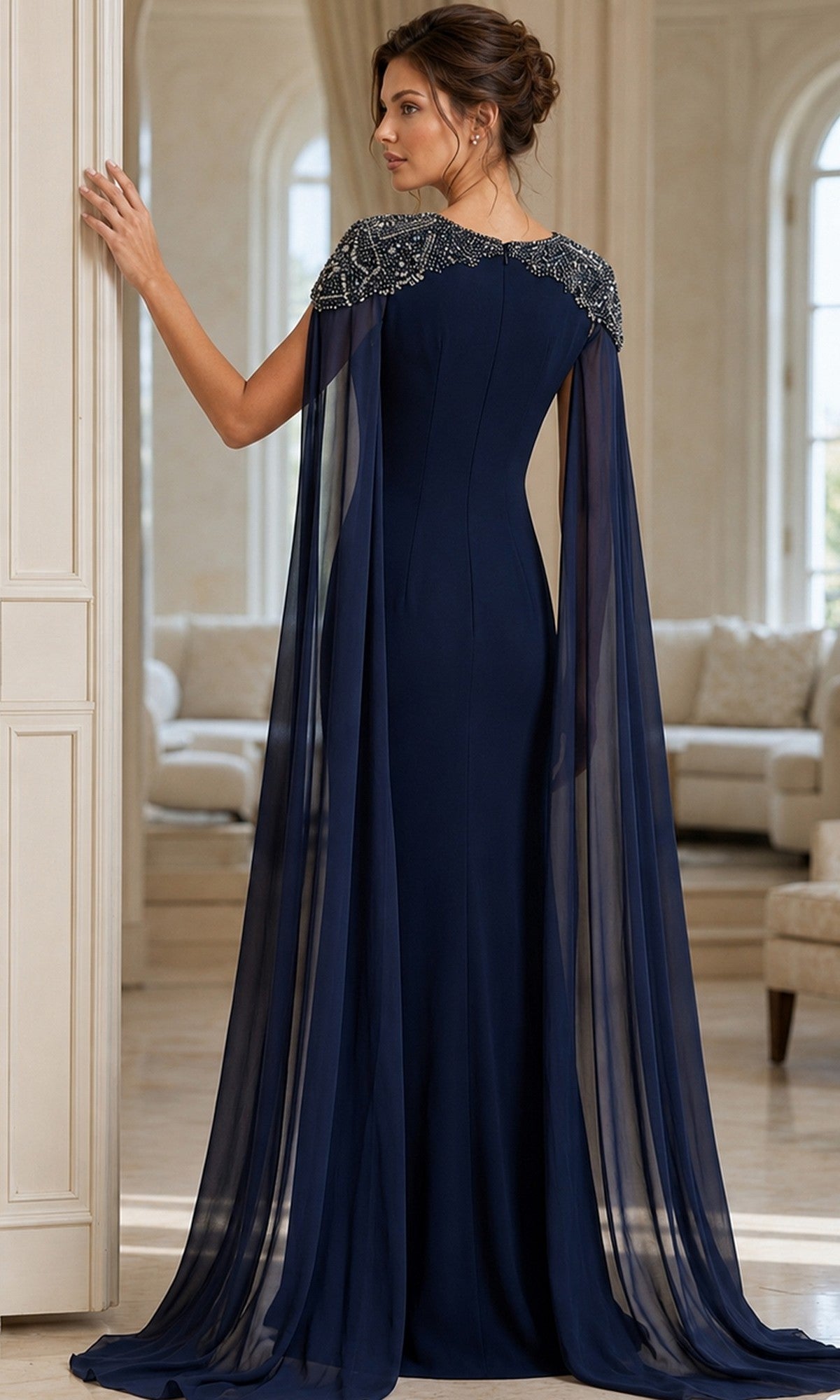 A woman stands indoors with her back to the camera, wearing the Long Formal Dress: Jovani 40000—an elegant navy blue gown featuring sheer chiffon cape sleeves and beaded shoulders.