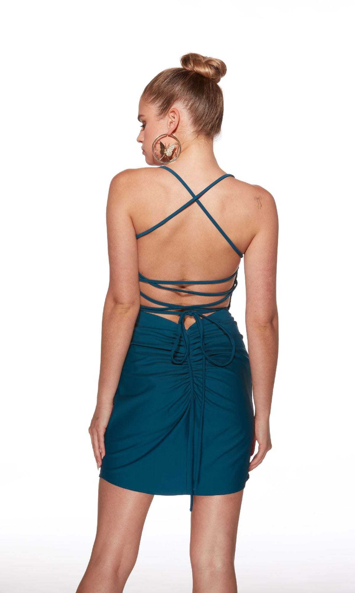 Woman with hair in a high bun stands with her back to the camera, wearing the Alyce 40021 strappy open-back short hoco dress in teal. Features ruched detailing and tie accents—perfect for making a statement at your next event.
