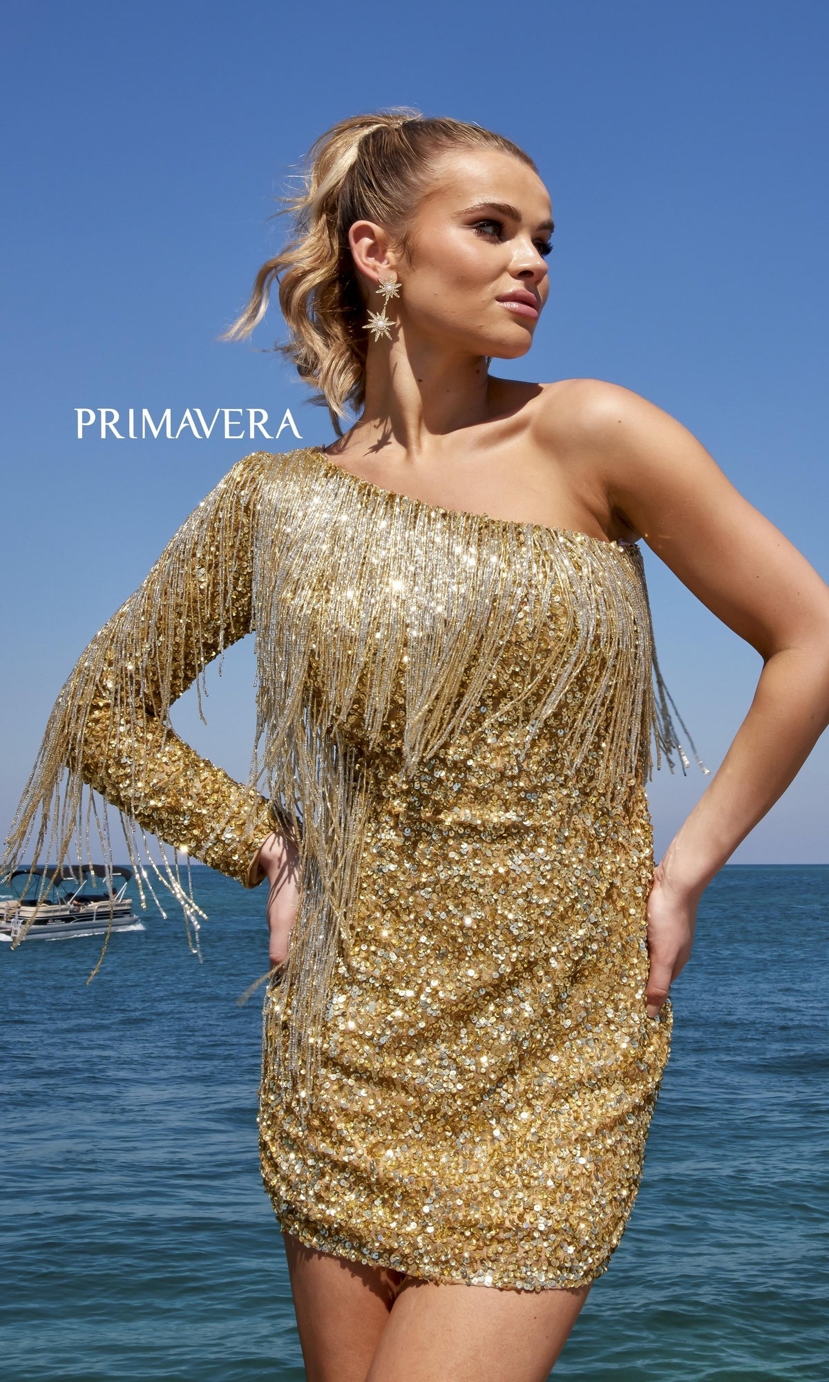 A woman stands by the ocean under a clear blue sky, wearing the One Long-Sleeve Fringed Sequin Party Dress 4003.