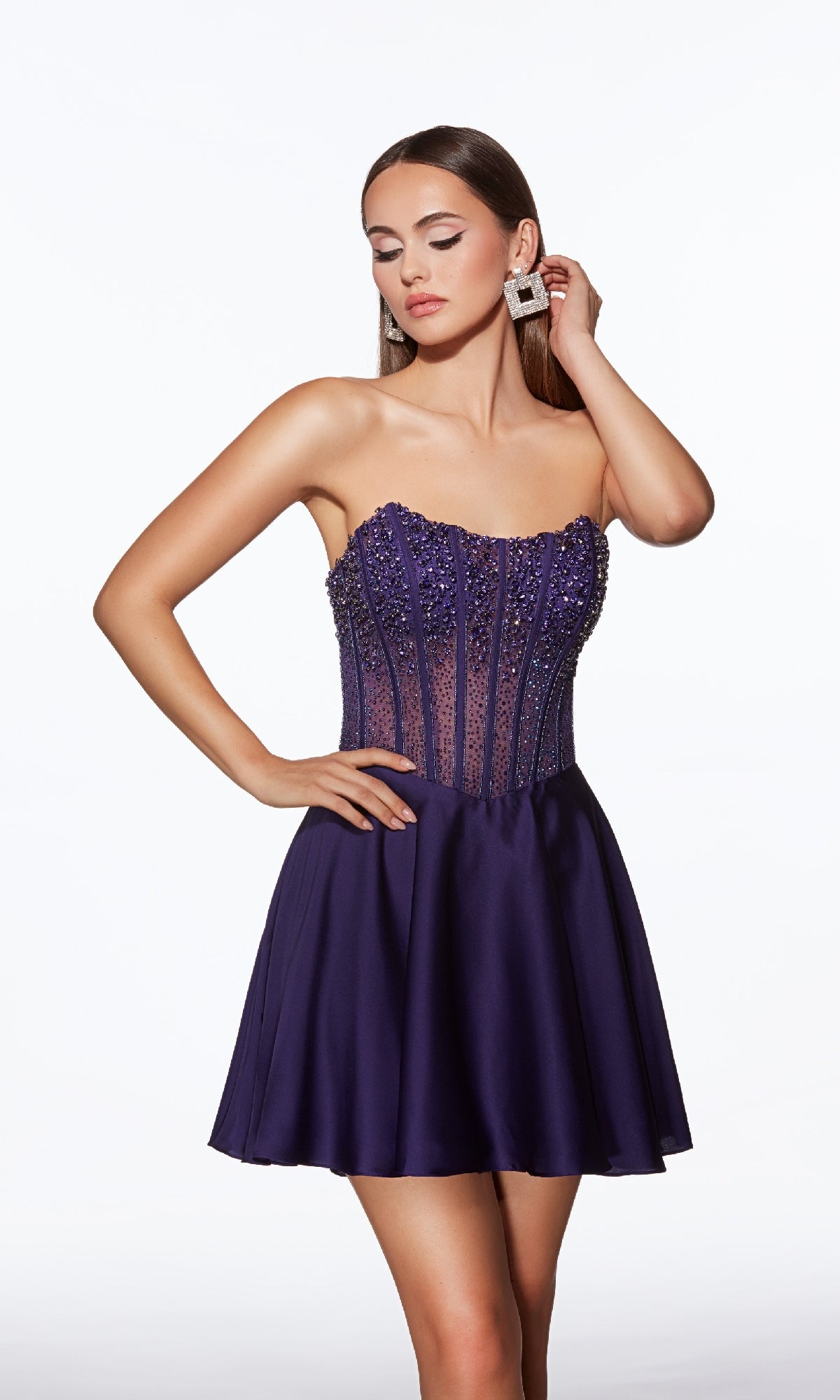 Woman in Alyce 40101 Strapless Short Corset Hoco Dress, featuring a bead-embellished bodice and flared skirt, poses with one hand on her hip and the other touching her earring against a white background.