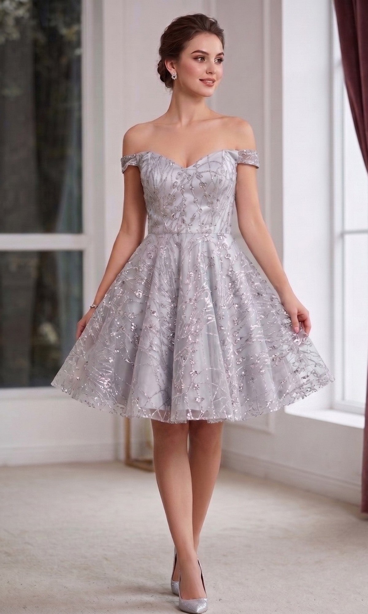A woman wearing the Chicas 4021 short homecoming dress in silver, featuring an off-the-shoulder sweetheart neckline, knee-length hemline, sheer overlay, and floral details, stands indoors by a window with burgundy curtains.