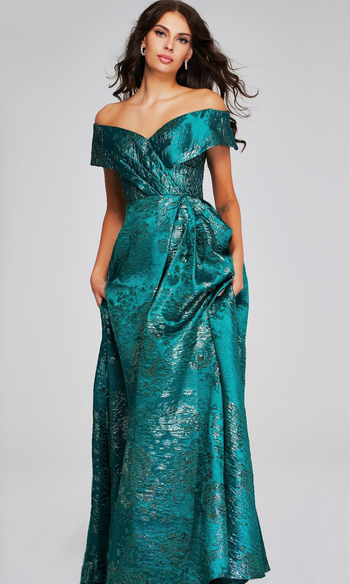 A woman models the Jovani 40296 long formal dress—an off-the-shoulder metallic teal gown with a textured pattern and gathered waist detail—against a plain background.