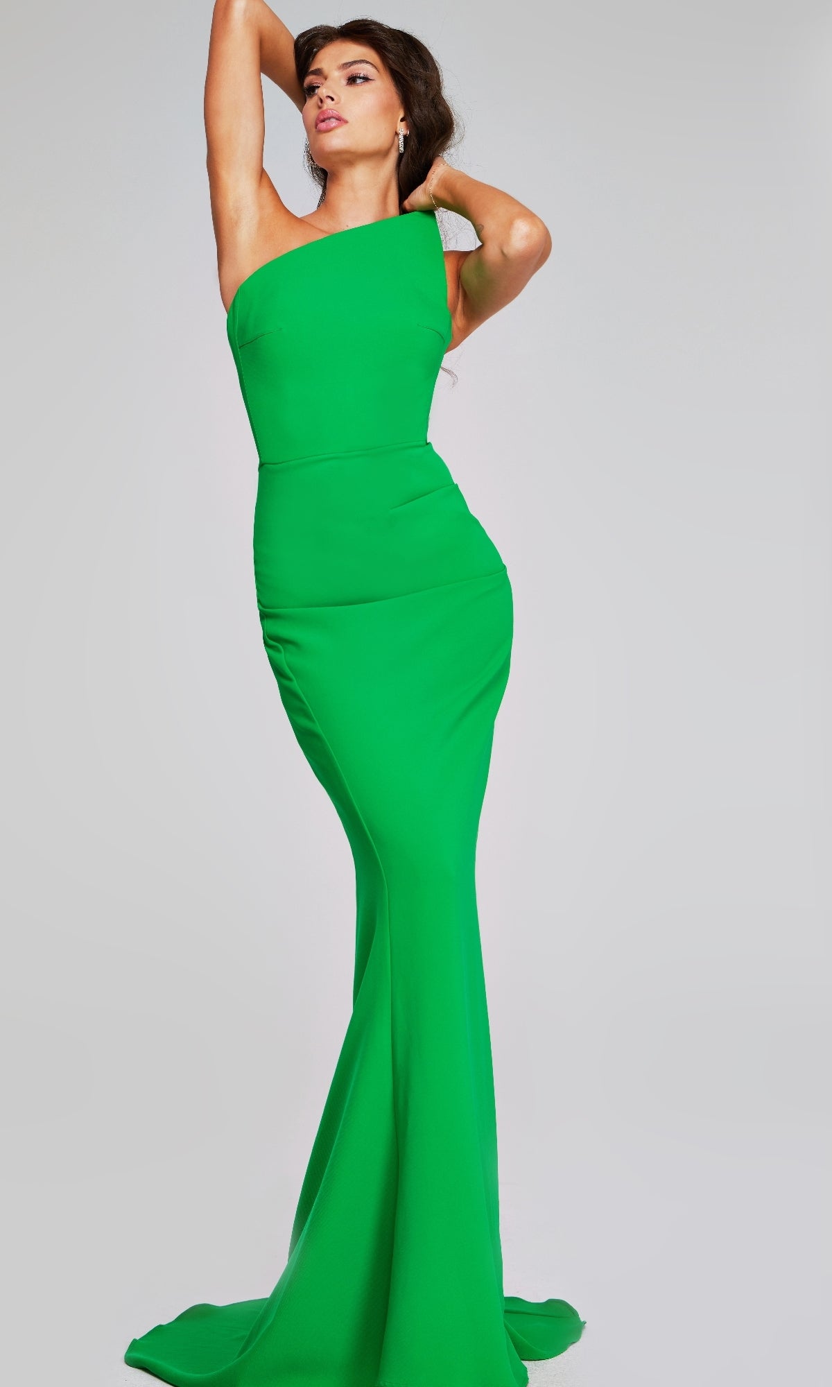 A woman poses in a green Jovani 40301 Asymmetrical Strapless Formal Gown with a floor-length mermaid skirt against a plain light gray background.