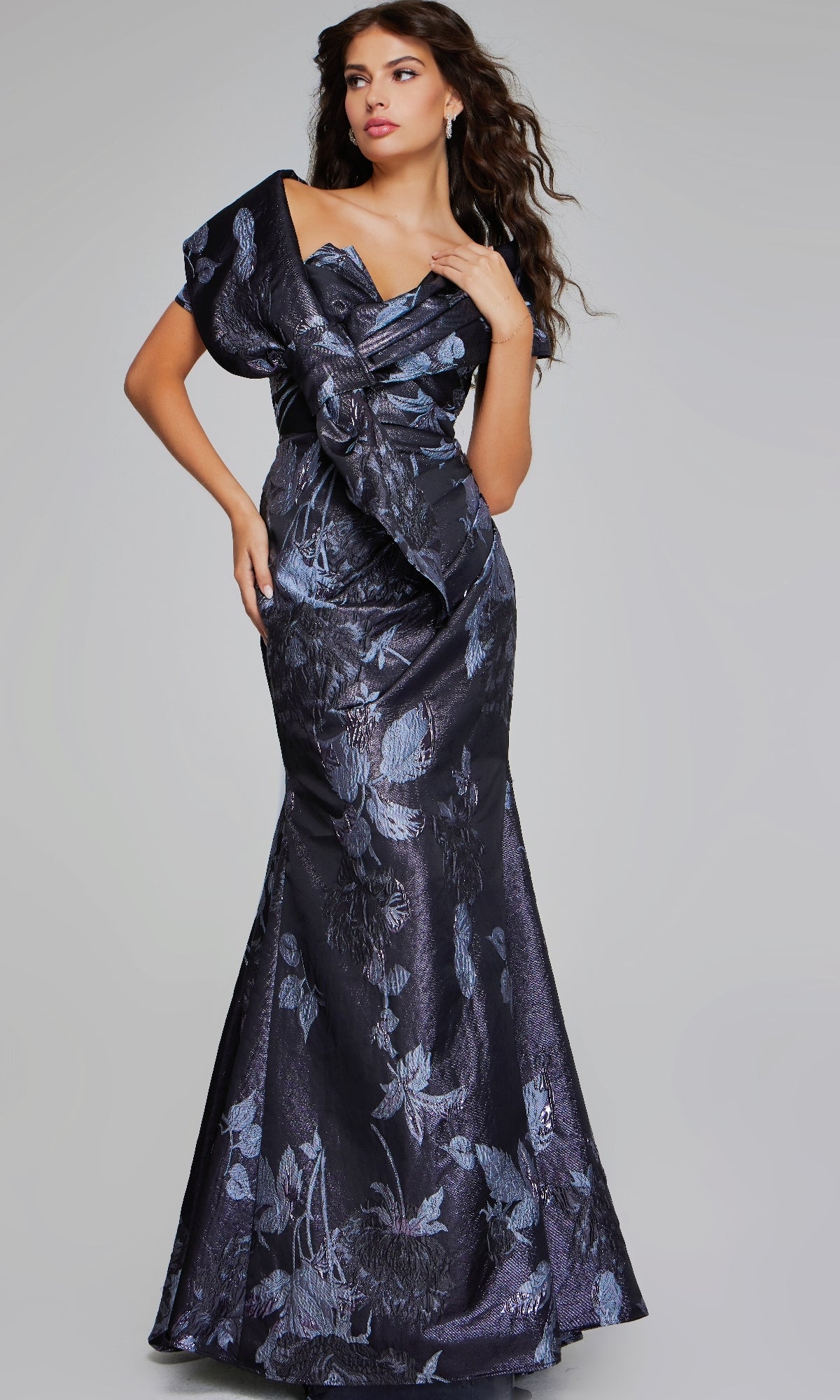 A woman models the Jovani 40309 long formal dress, a floor-length fitted navy gown with floral print and an asymmetrical ruffled neckline, highlighting its elegant mermaid silhouette against a plain background.