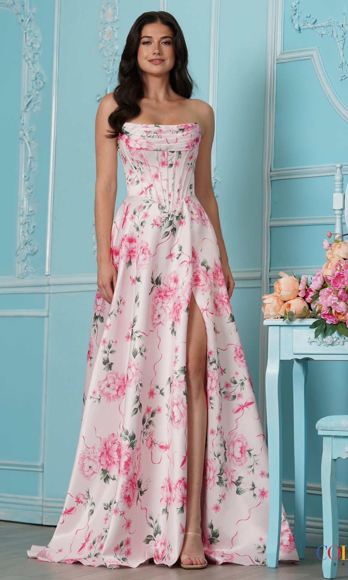 A woman wearing a pink Long Prom Dress: Colors Dress 4031, featuring a strapless floral corset-style bodice, a floor-length hem, and a high leg slit.