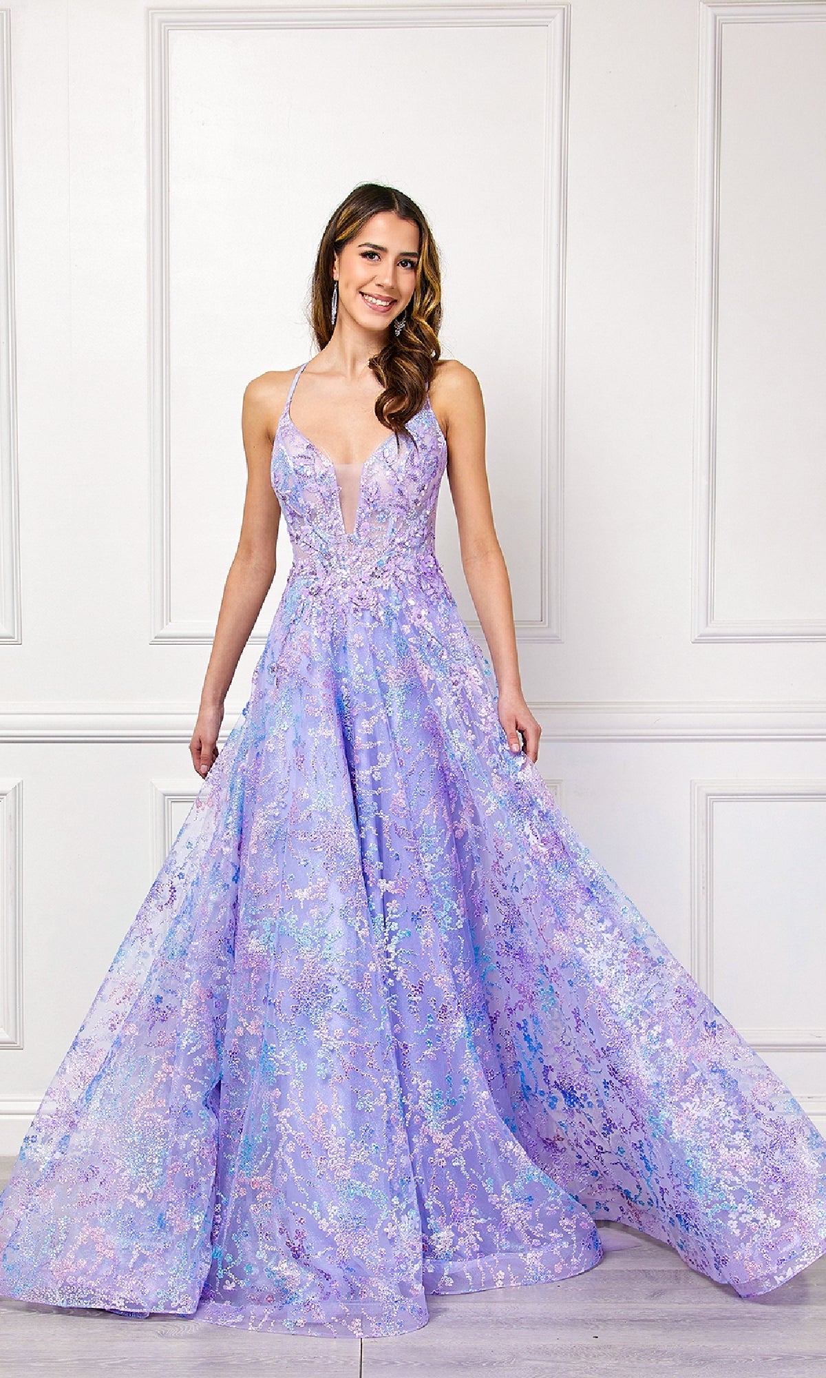 A woman stands indoors, smiling at the camera in an Amelia Couture 4050 Embellished Long Prom Dress featuring a sleeveless lavender A-line silhouette, deep V neckline, and floral patterns.