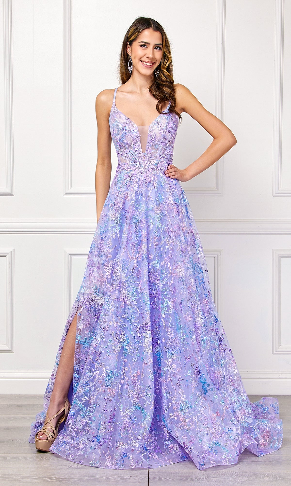 A woman stands indoors wearing the Amelia Couture 4050 Embellished Long Prom Dress, a sleeveless, floor-length lavender A-line gown with a plunging neckline, floral details, and a high slit, paired with gold heels.