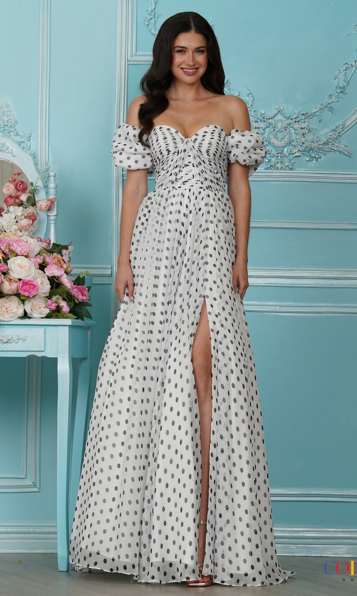 A woman wears a white, off-the-shoulder, floor-length polka dot Long Prom Dress: Colors Dress 4053 featuring a high leg slit.
