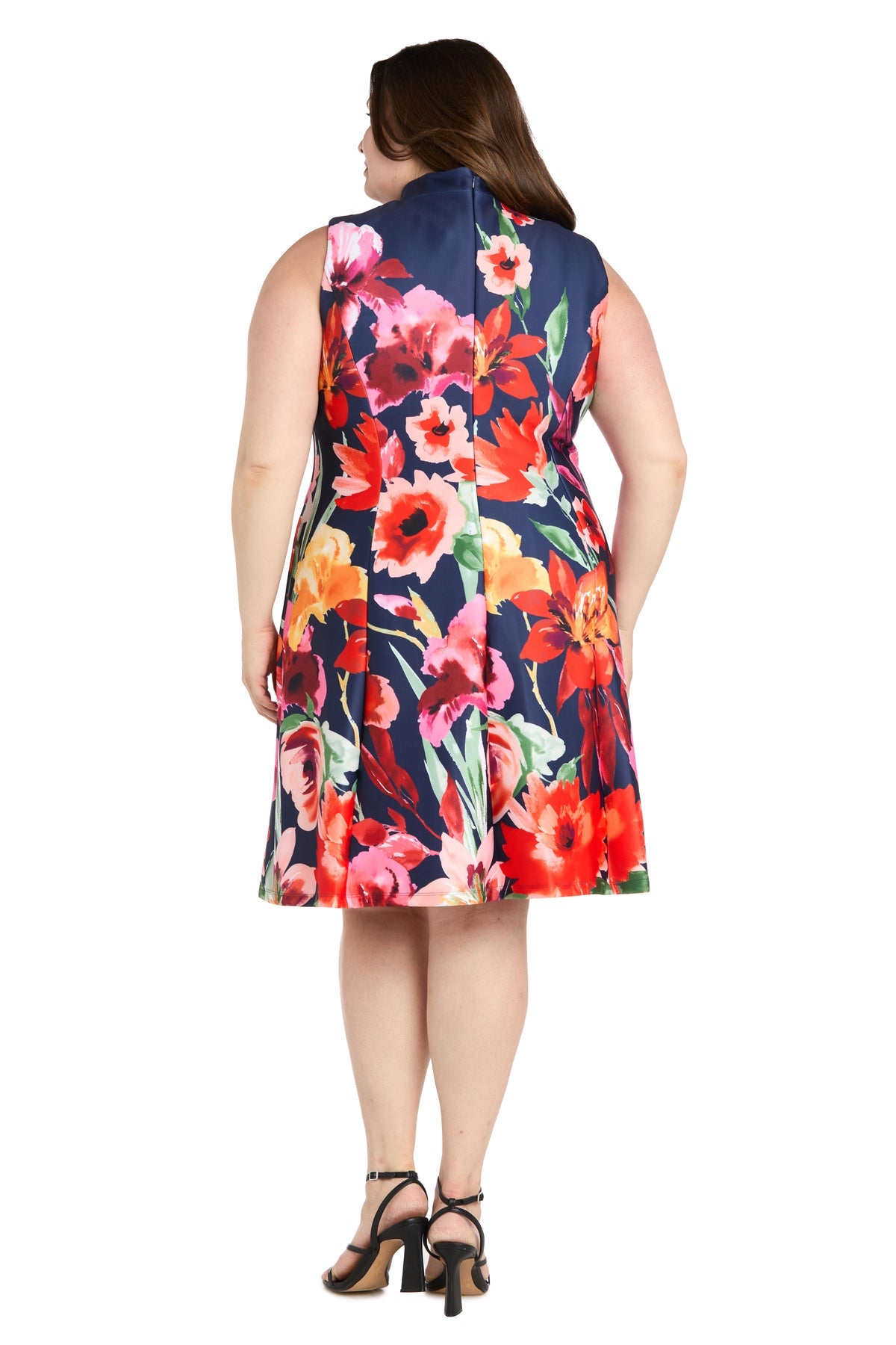 A woman showcases the back of the R&M Richards 4056W Plus-Size Wedding Guest Dress—a sleeveless, knee-length floral print dress—styled with black heeled sandals for a semi-formal look.