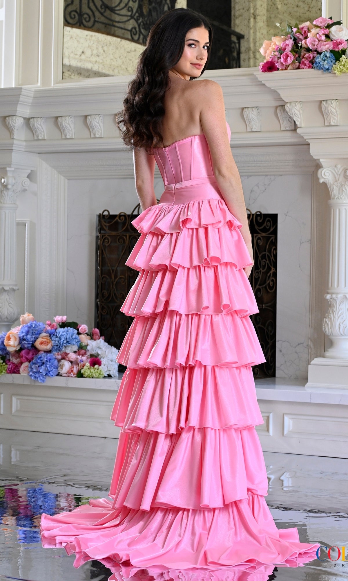 A person wearing a pink Long Prom Dress: Colors Dress 4061 with a strapless sweetheart neckline, corset bodice, and a tiered, ruffled floor-length skirt.