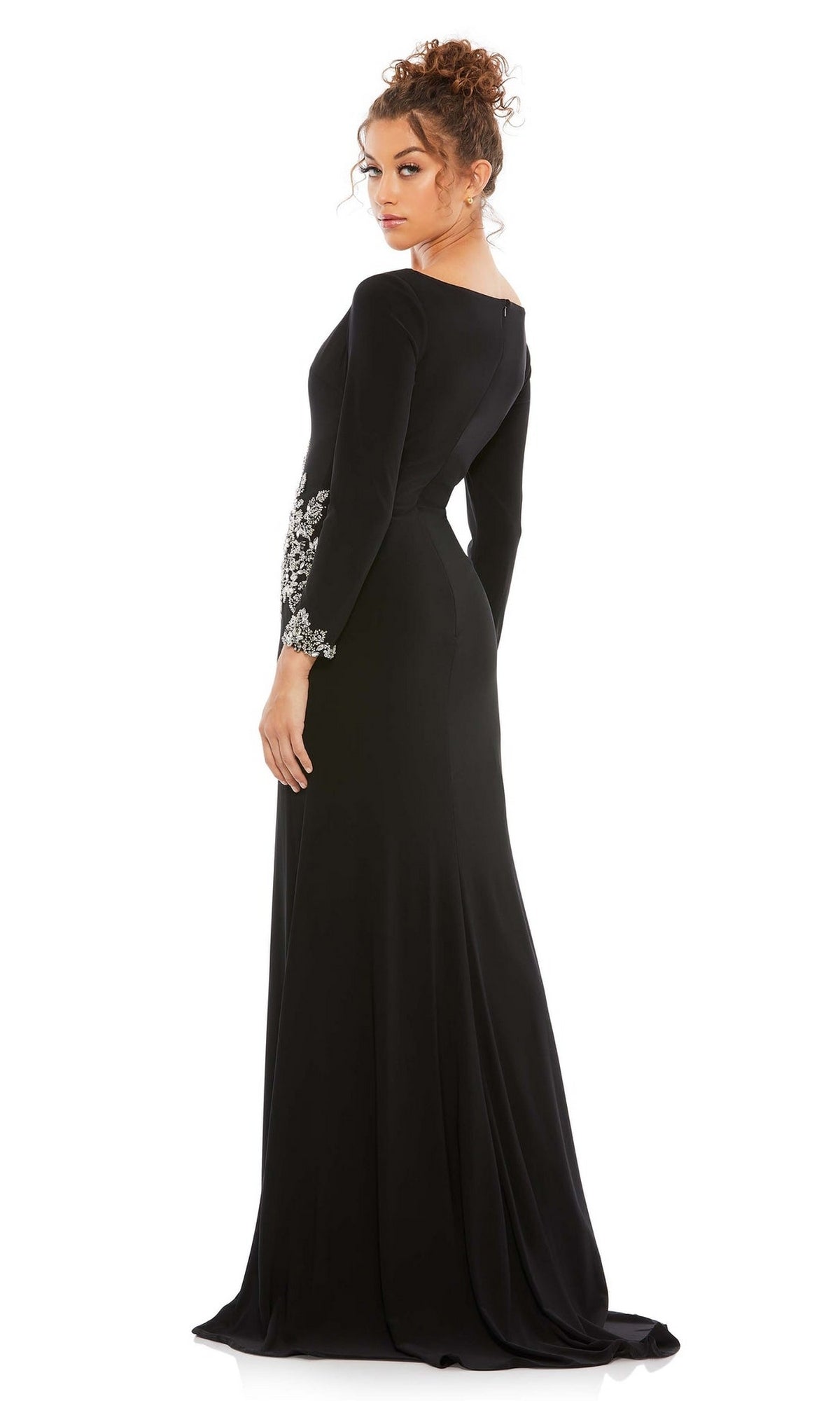 A woman wears the Long Formal Dress 41016 by Mac Duggal—a black, long-sleeved fitted gown with silver waist embellishments—standing and looking over her shoulder.