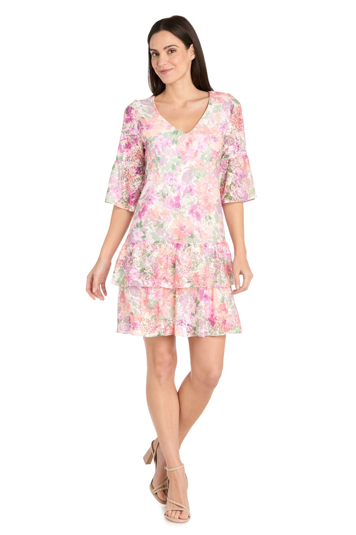 A woman models the R&M Richards 4107 Short Ivory Floral Party Dress, featuring ruffled sleeves and hem, paired with nude sandals—an elegant choice for casual cocktail events against a white backdrop.