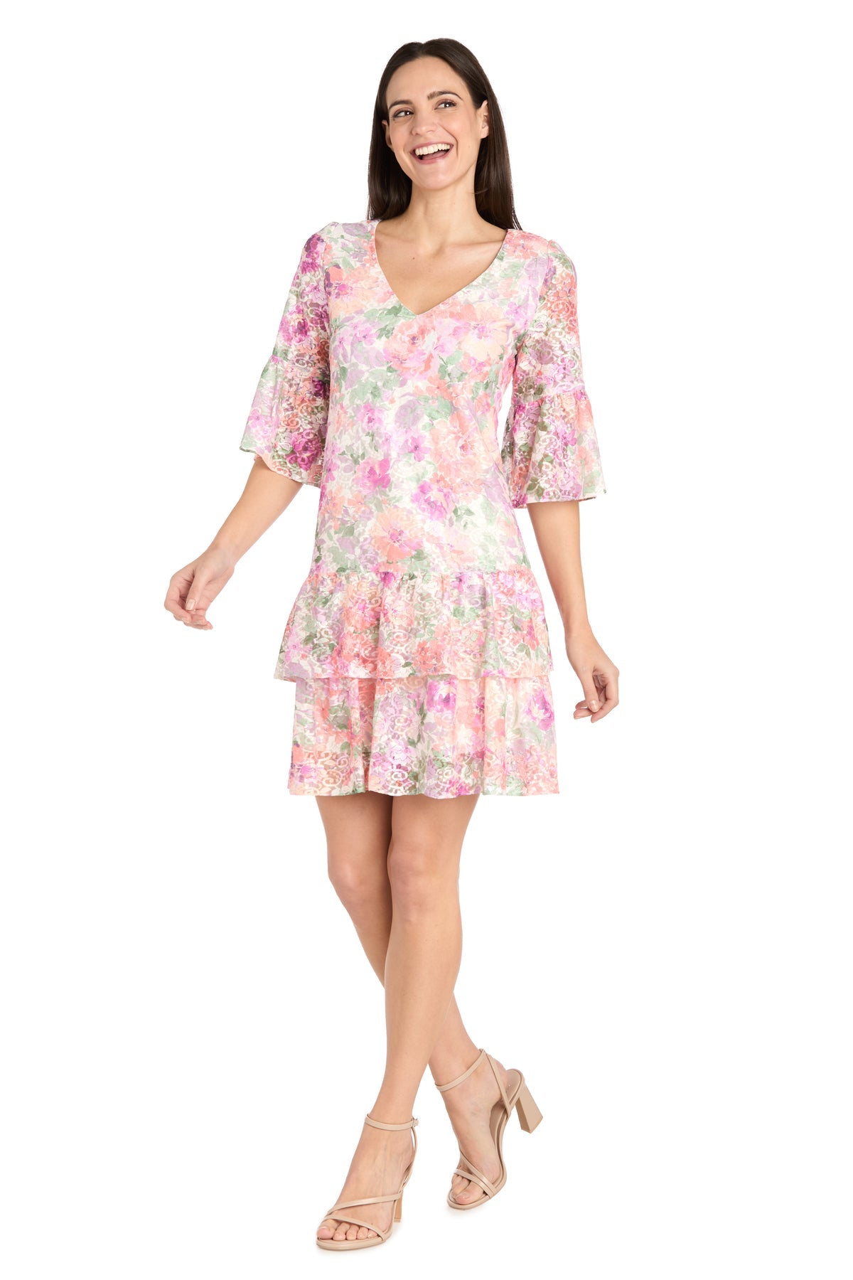 A woman wears the Short Ivory Floral Party Dress by R&M Richards (style 4107) featuring ruffled sleeves and hem, paired with beige block-heeled sandals, standing against a white background.