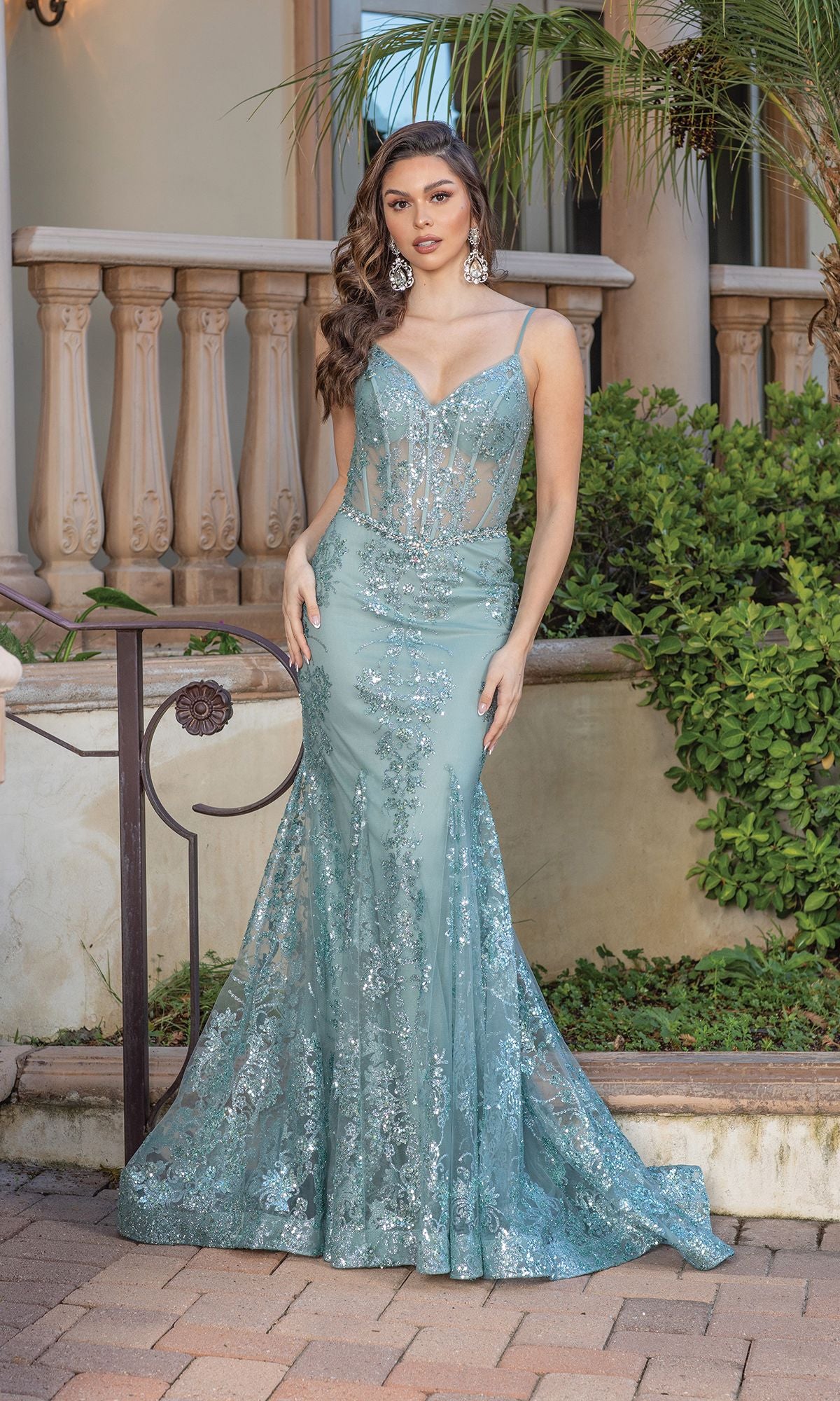 A woman stands outdoors near a stone railing and greenery, wearing the Long Sequined and Beaded Mermaid-Style Prom Dress—a light blue, floor-length gown featuring thin straps and shimmering beadwork.