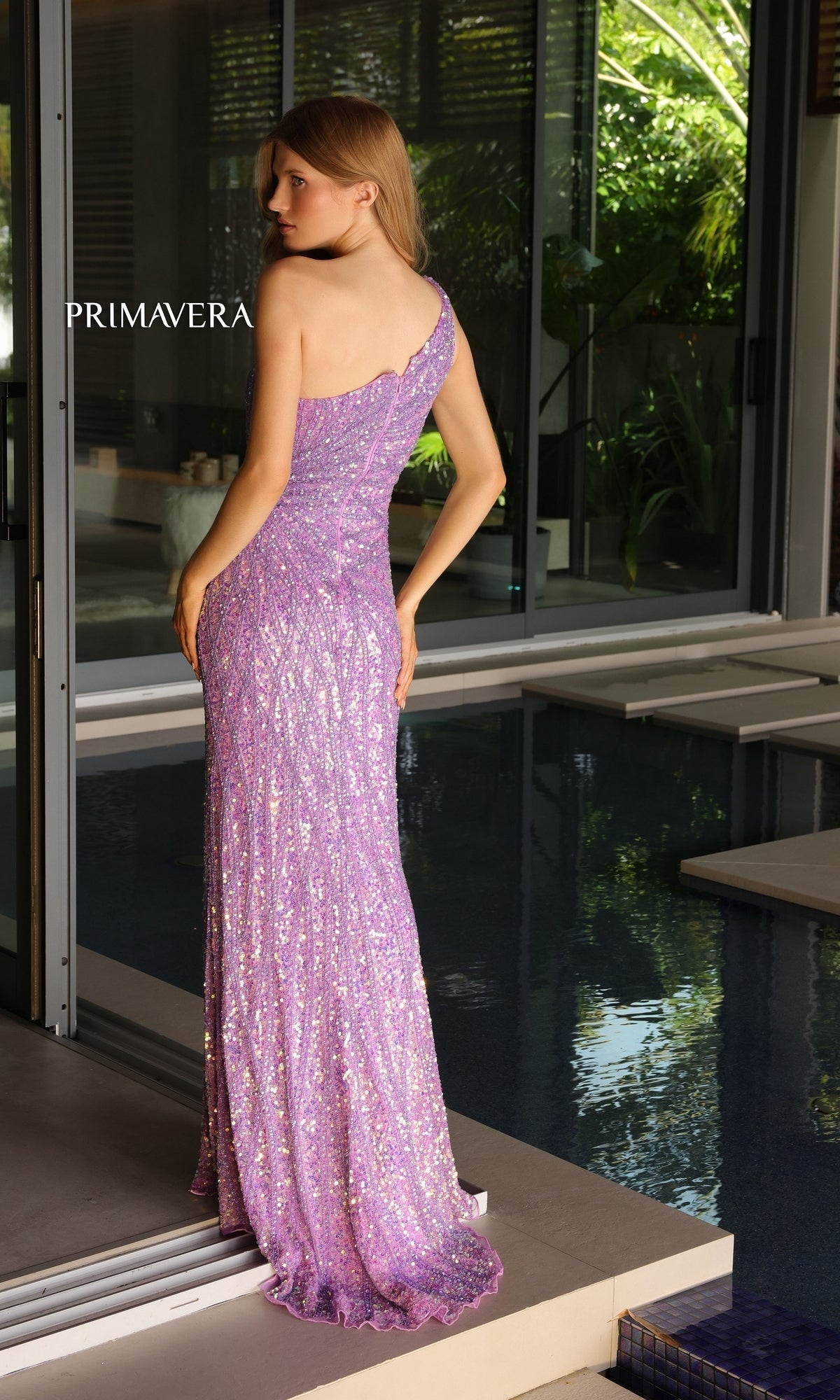 A woman poses by an indoor pool in the Primavera One-Shoulder Long Beaded Prom Dress 4133, a floor-length gown adorned with purple sequins.